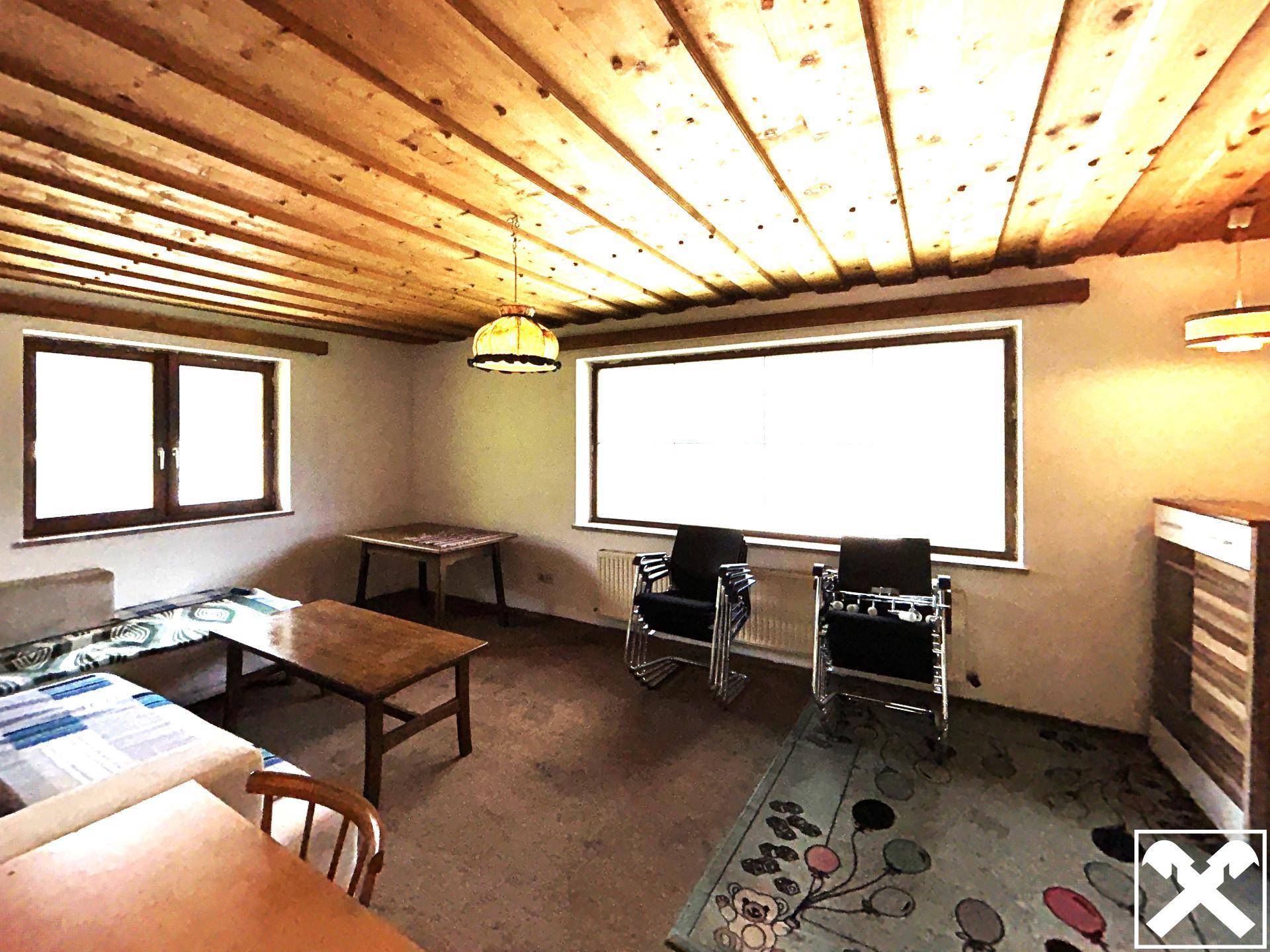 Rustikales Wohnzimmer mit Holzbalkendecke, Teppichboden und traditionellen Möbeln.