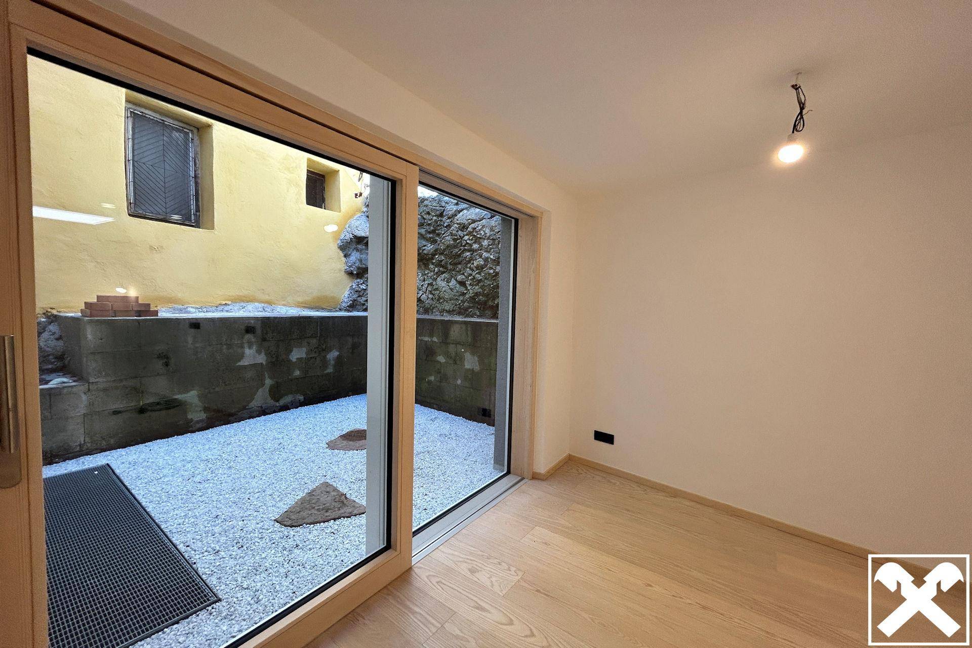 Helles Zimmer mit Holzboden und großen Schiebetüren, die zu einem kleinen Kieshof führen.