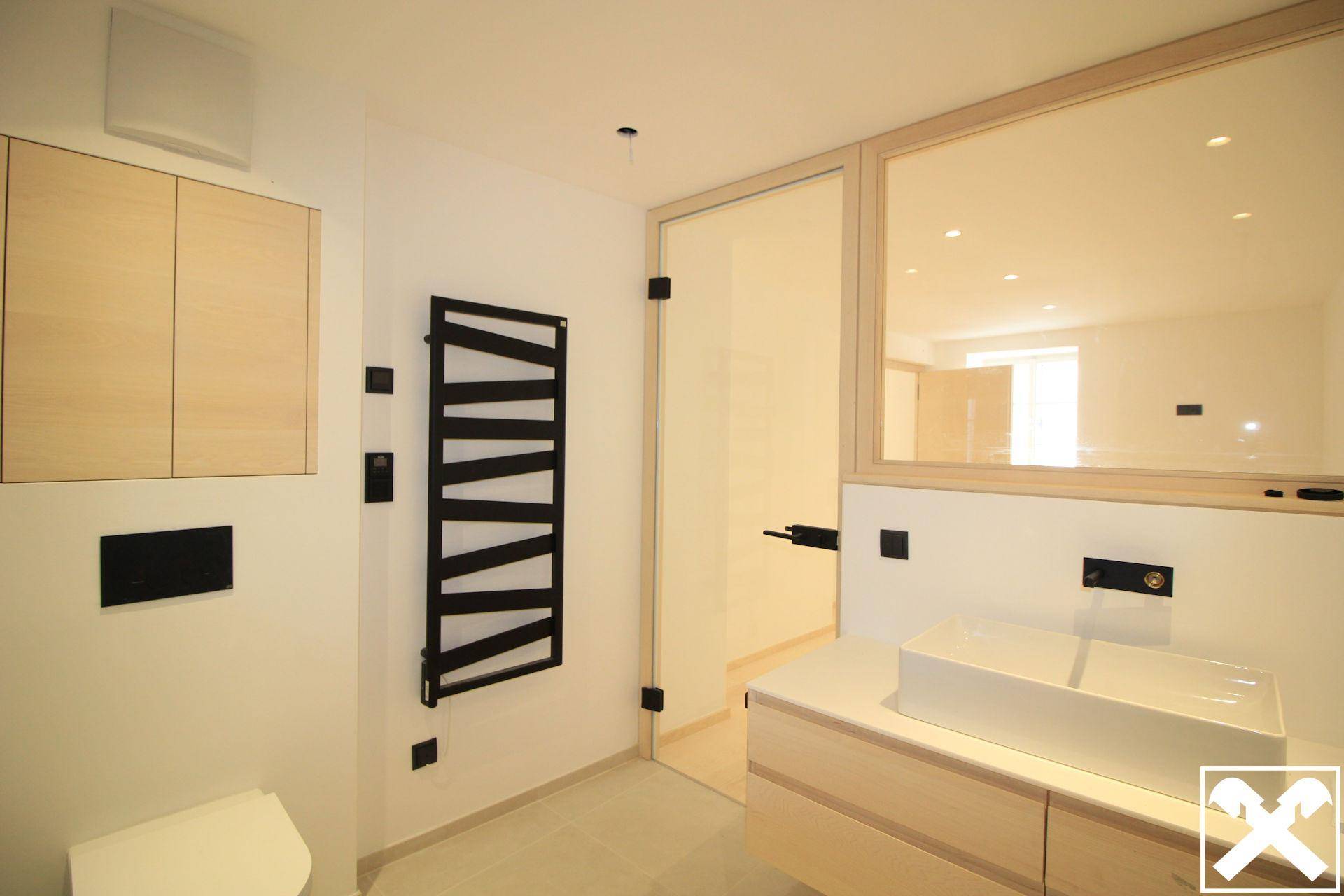Modernes Badezimmer mit hellem Holzwaschtisch, Wand-WC und schwarzem Handtuchheizkörper.