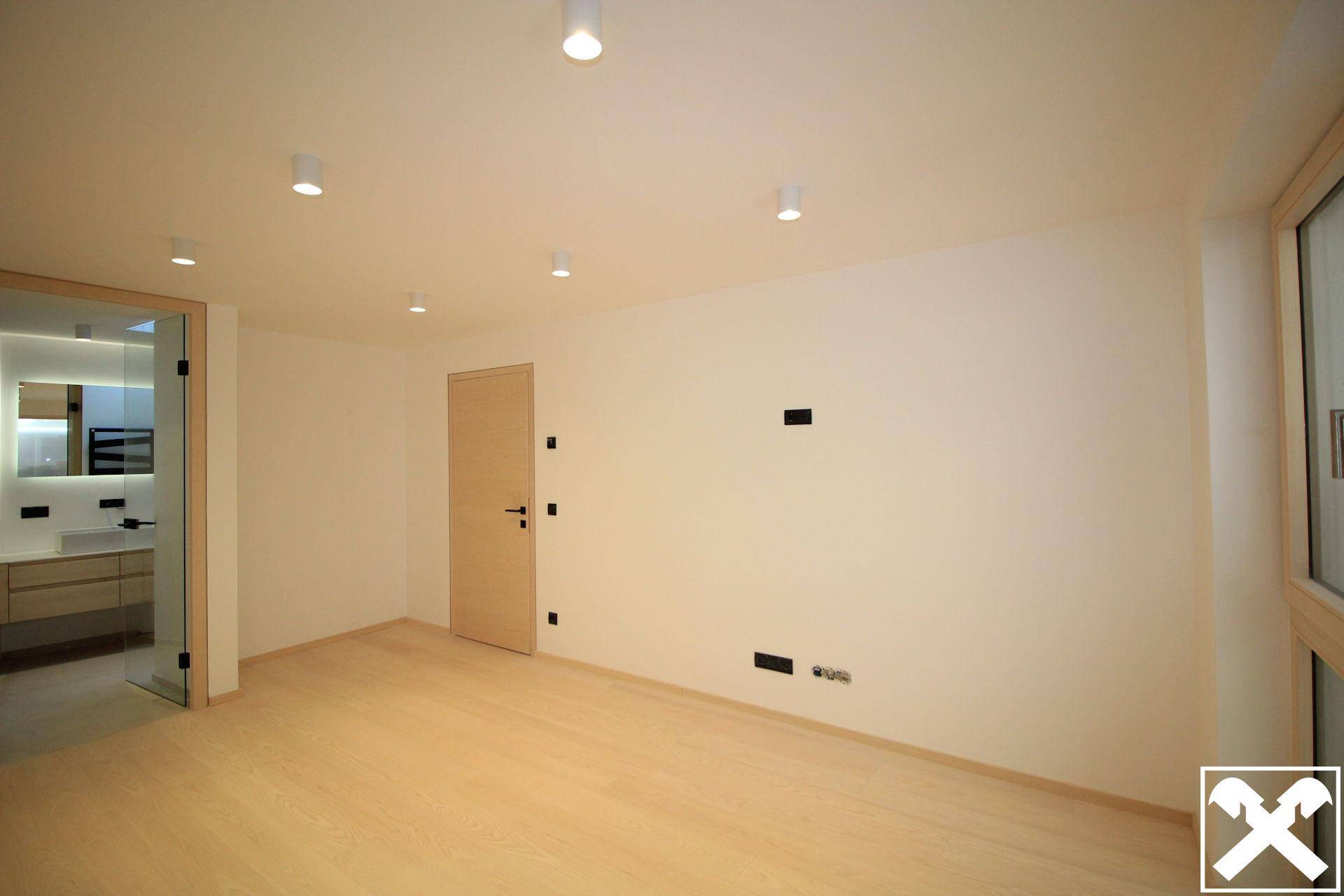 Helles Schlafzimmer mit Holzboden, weiß gestrichenen Wänden und direktem Zugang zu einem modernen Badezimmer.