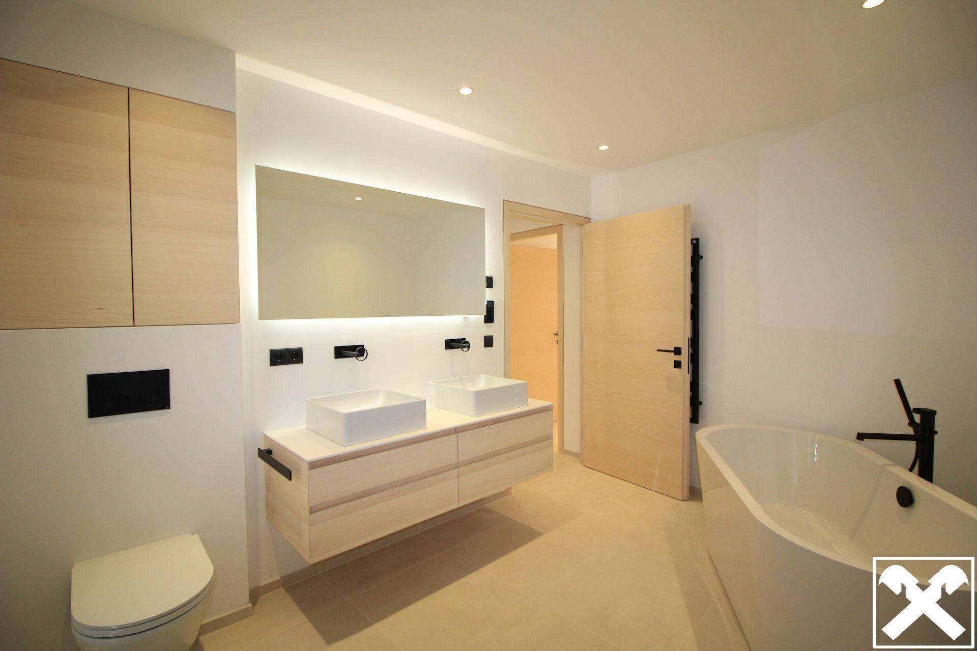 Elegantes Badezimmer mit freistehender Badewanne, Doppelwaschbecken und großem beleuchteten Spiegel.