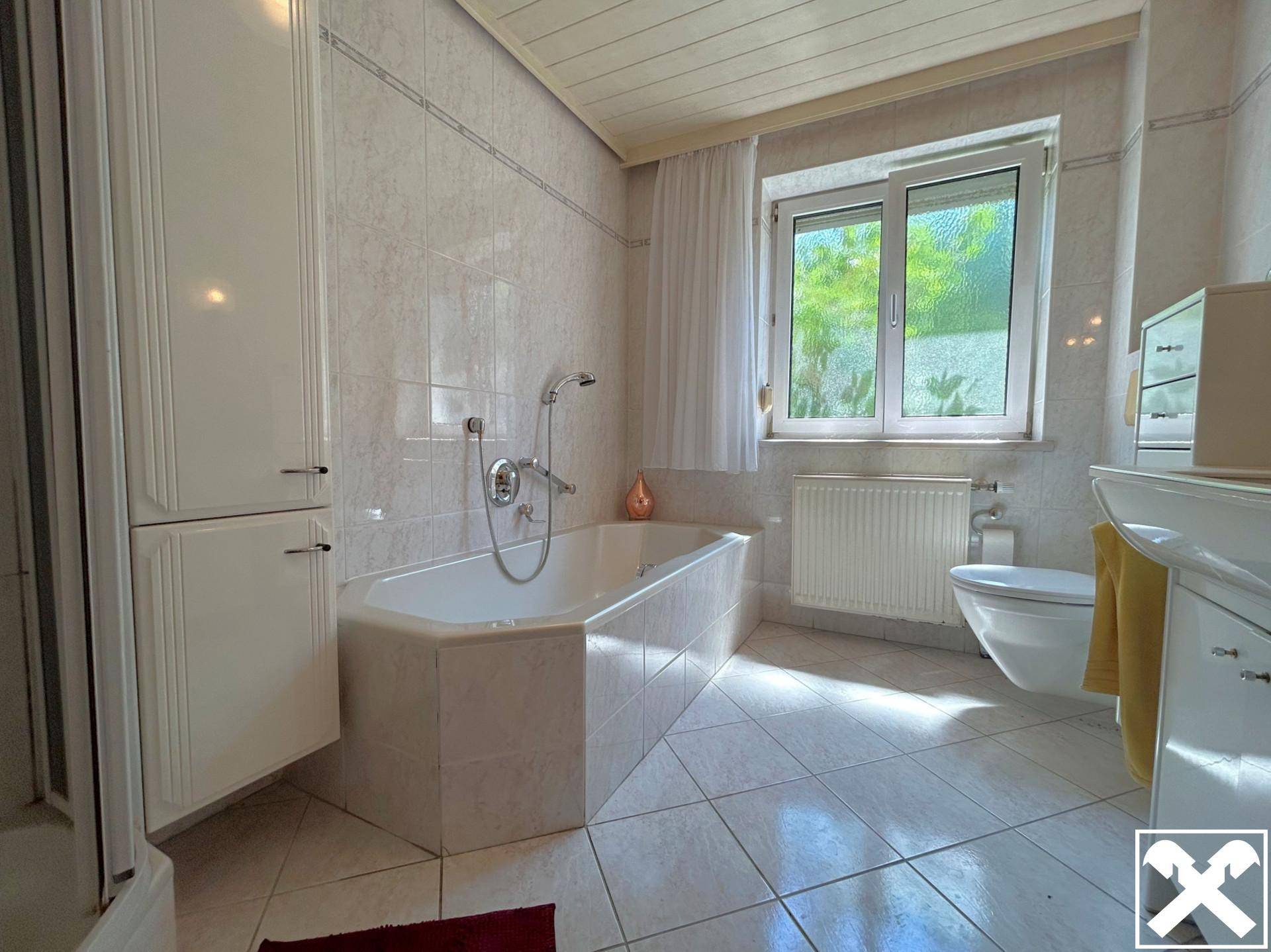 Helles Badezimmer mit Badewanne, Fliesenboden und Fenster für natürliches Licht.