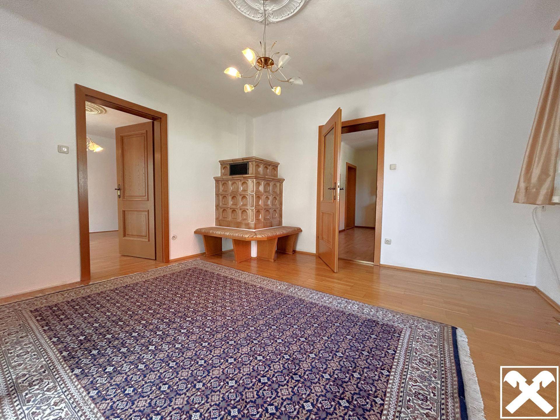 Geräumiges Wohnzimmer mit Kachelofen, Holzboden und dekorativer Deckenrosette.