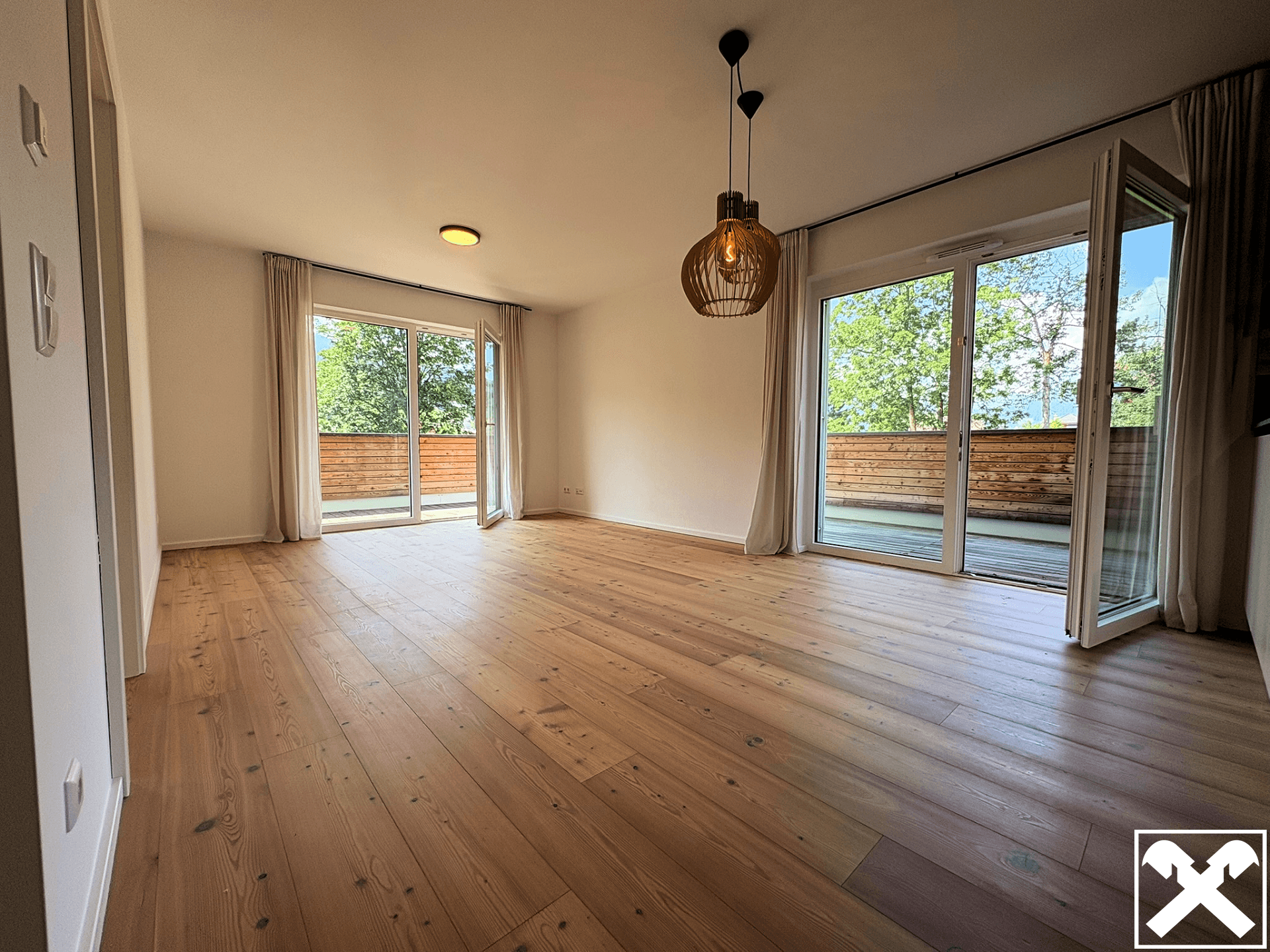 Helles Wohnzimmer mit Holzboden und großzügigem Zugang zu einem breiten Balkon.