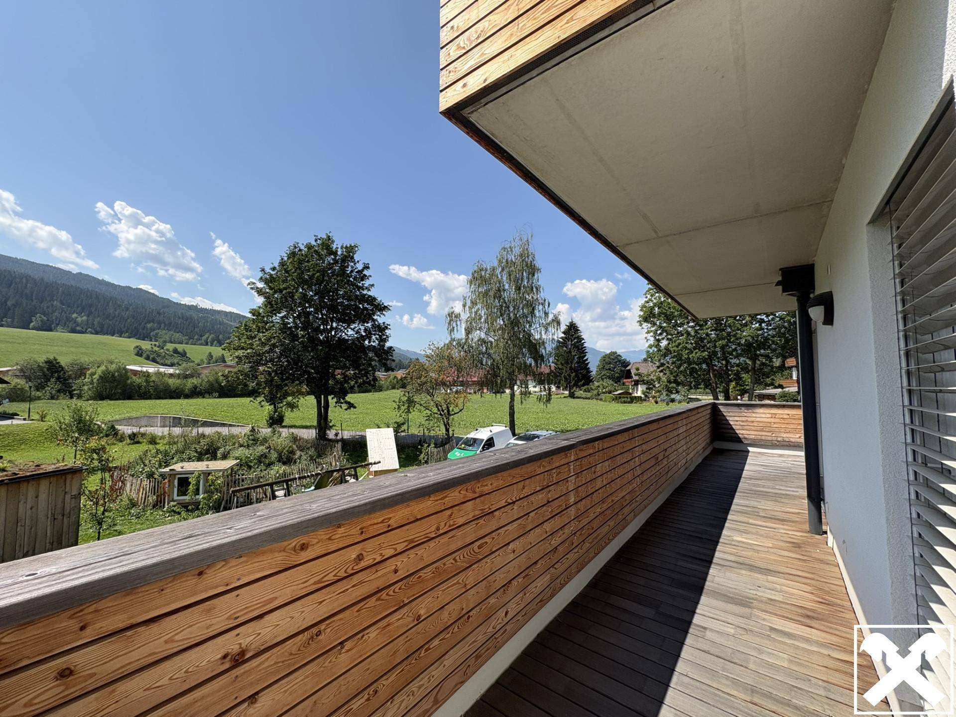 Geräumiger Holzbalkon mit weitem Blick auf die grüne Landschaft und die umliegenden Berge.