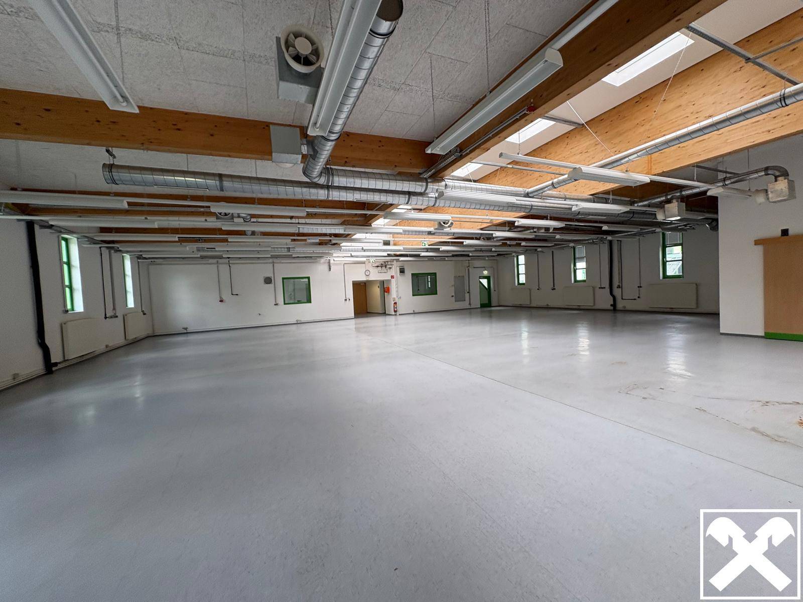 Weitläufige Produktionshalle mit hohen Decken, sichtbaren Lüftungsanlagen und vielen Fenstern für Tageslicht.