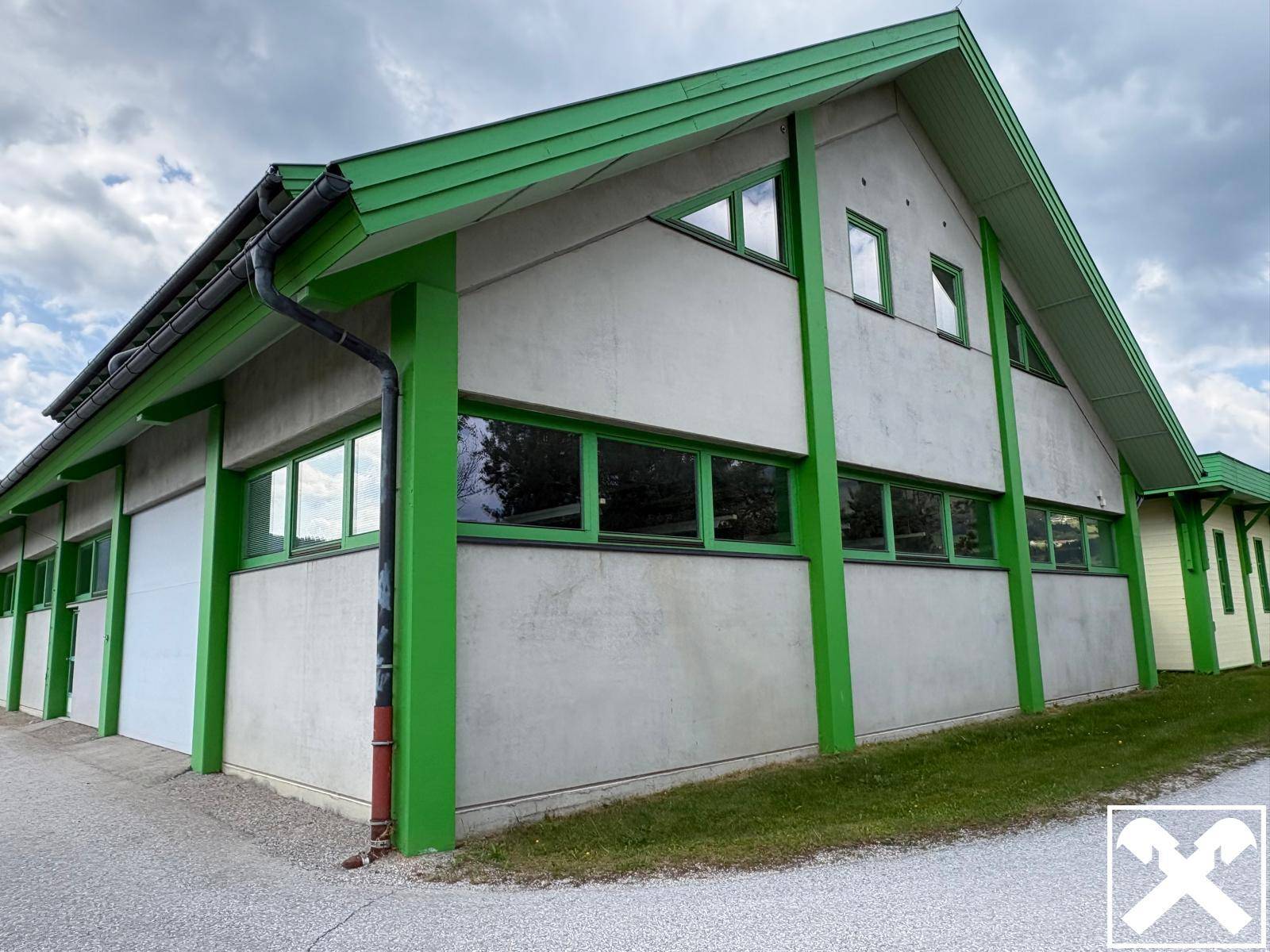 Außenansicht des Gebäudes mit markanten grünen Fensterrahmen und einem Satteldach unter bewölktem Himmel.