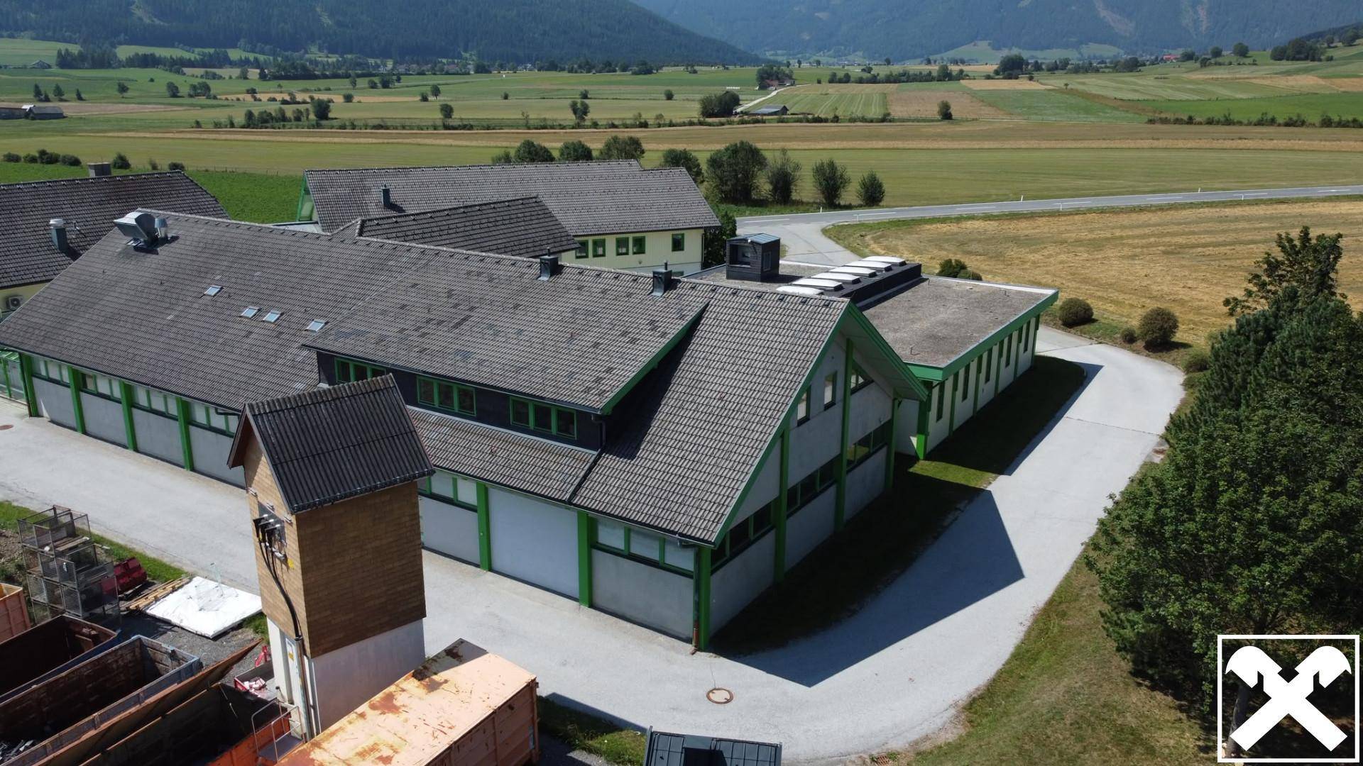 Luftaufnahme des Gebäudekomplexes in einer ländlichen Umgebung mit weiten Feldern und Bergen im Hintergrund.