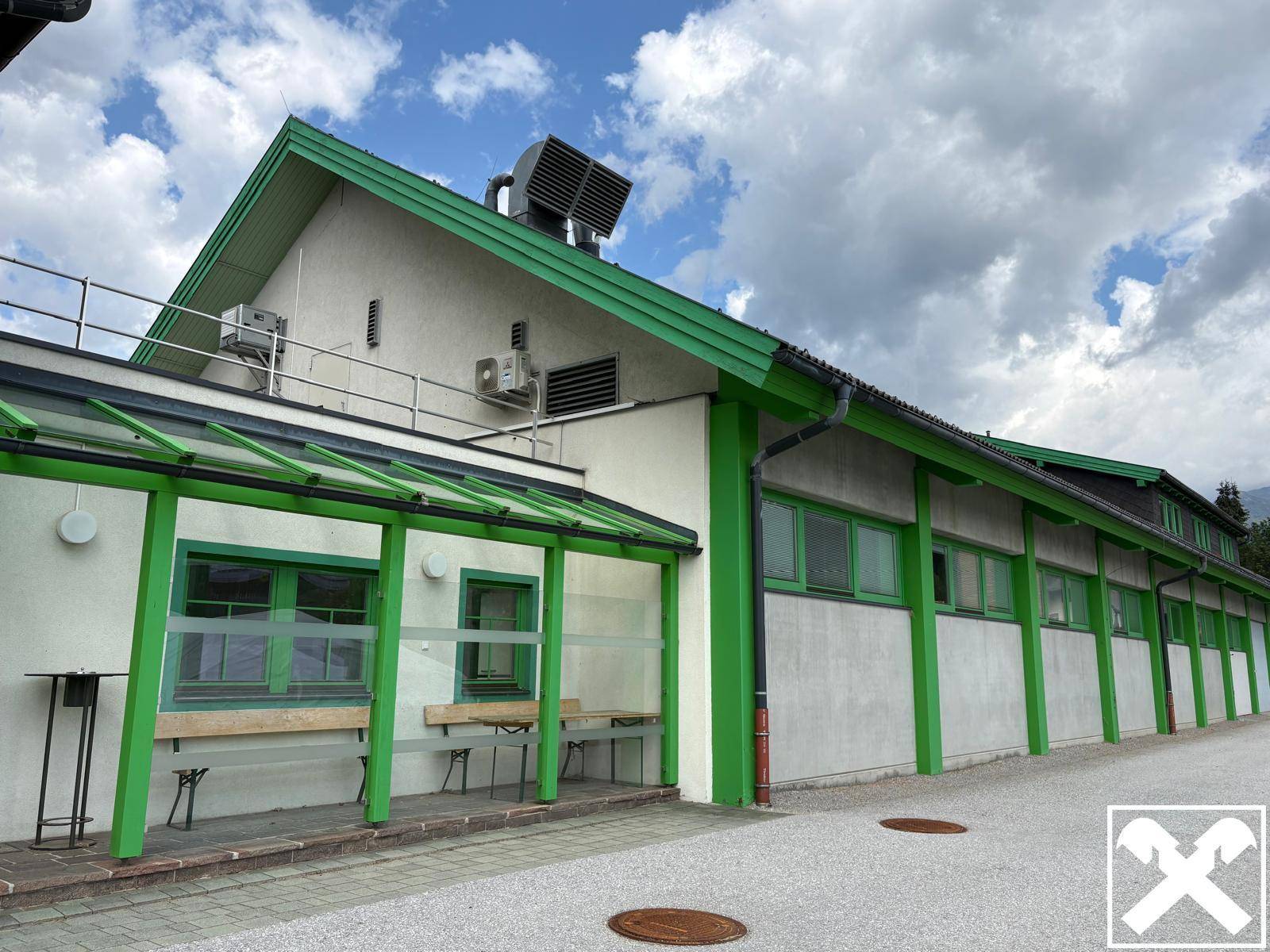 Seitenansicht des Gebäudes mit grünen Akzenten, Klimaanlagen an der Fassade und einem überdachten Eingangsbereich.