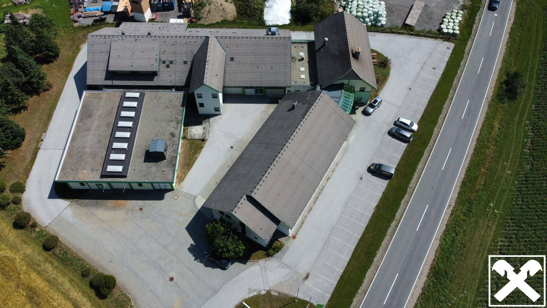 Draufsicht auf den Gebäudekomplex mit Parkplätzen und angrenzender Straße, umgeben von Feldern.