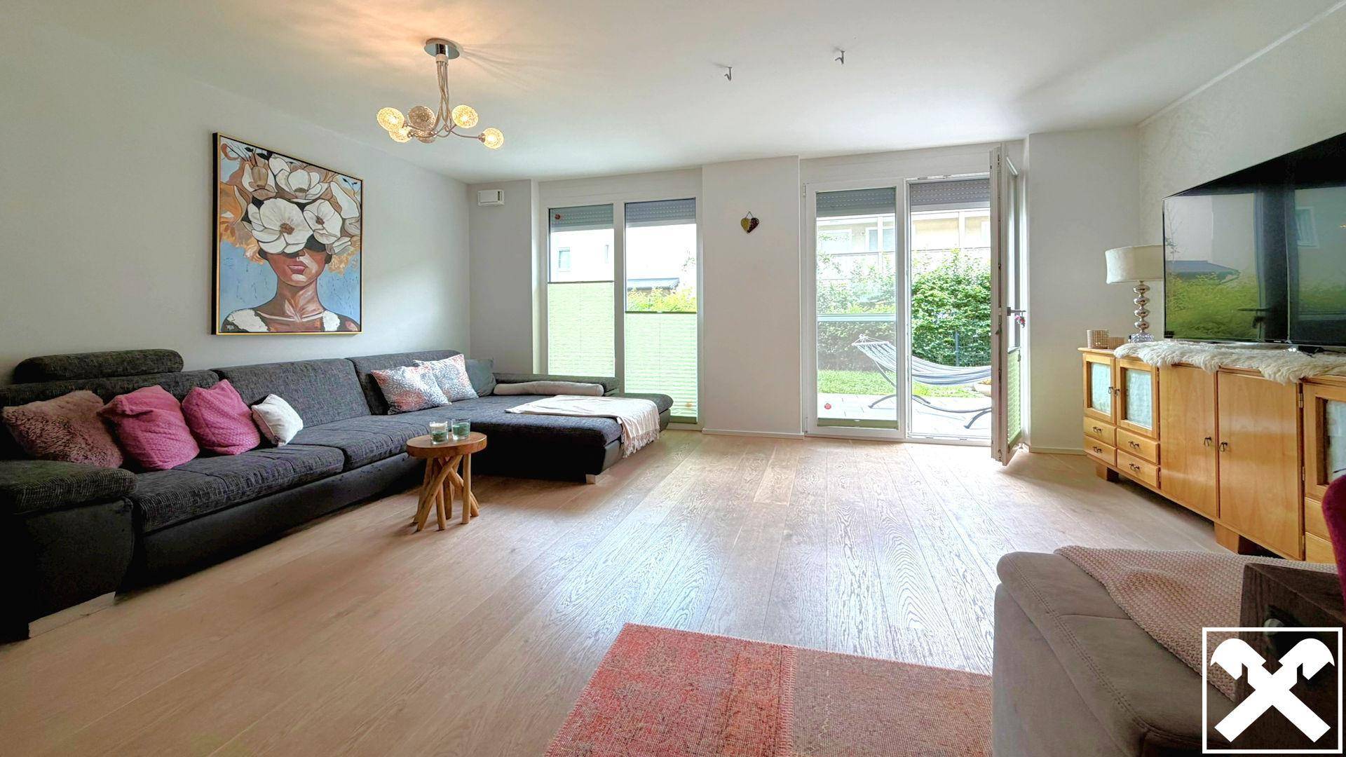 Helles Wohnzimmer mit großem Sofa, Holzboden und Zugang zur Terrasse und zum Garten.