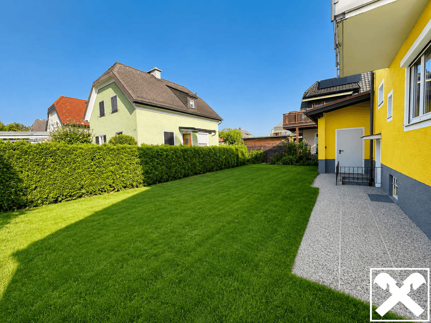 Gepflegter grüner Gartenbereich mit Rasenfläche und hoher Hecke neben dem Haus.