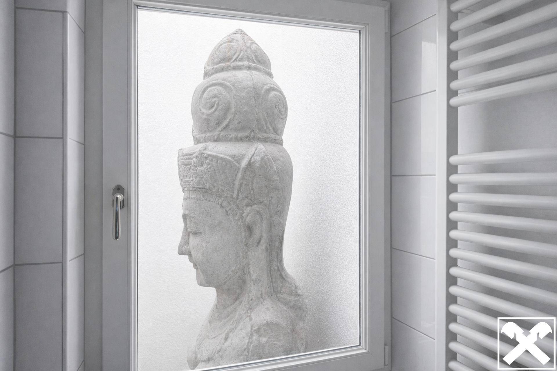 Badezimmerfenster mit undurchsichtigem Glas und dekorativer Statue, daneben ein Handtuchheizkörper.