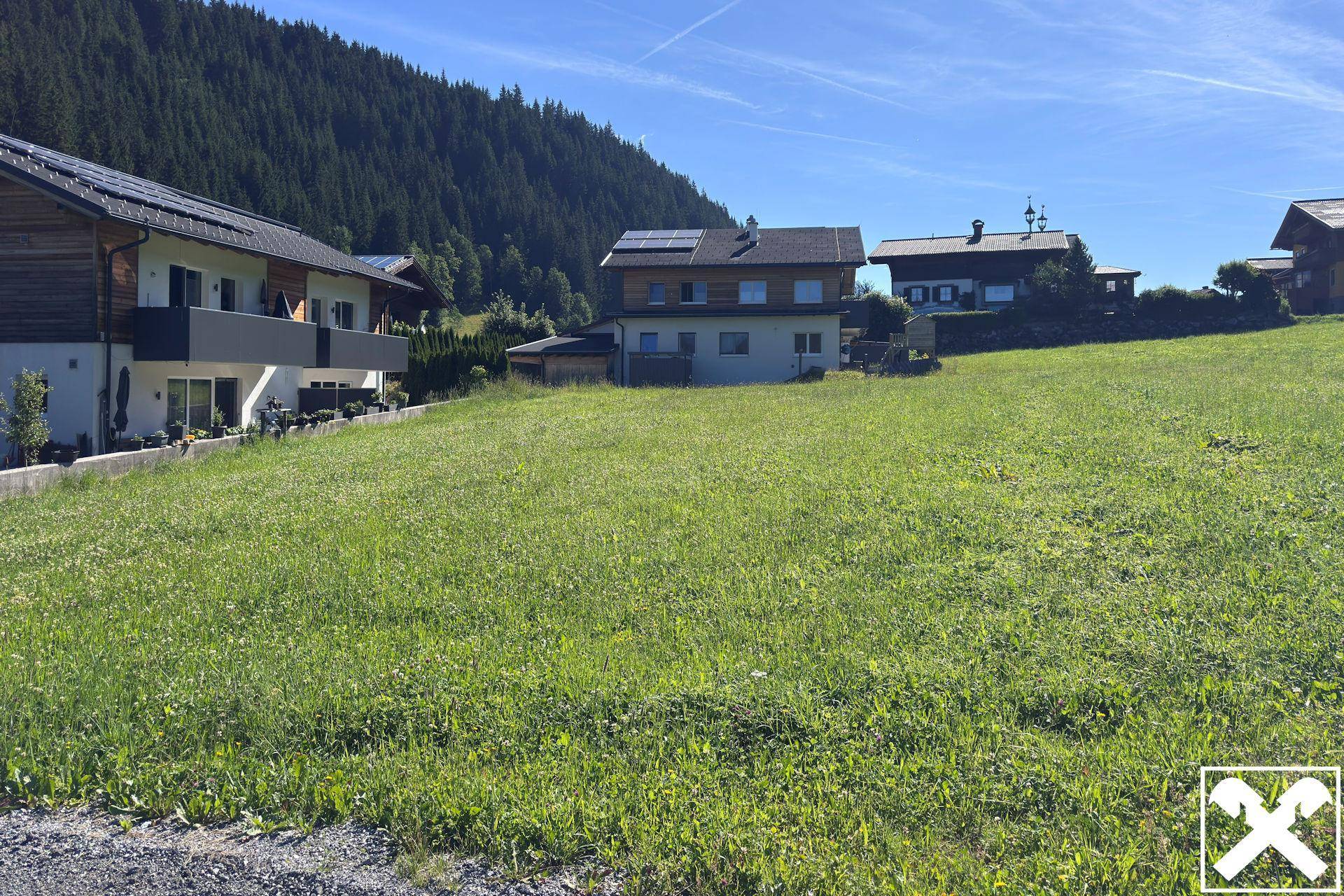 Grünes Grundstück mit Blick auf benachbarte Wohnhäuser und die umliegende Berglandschaft.