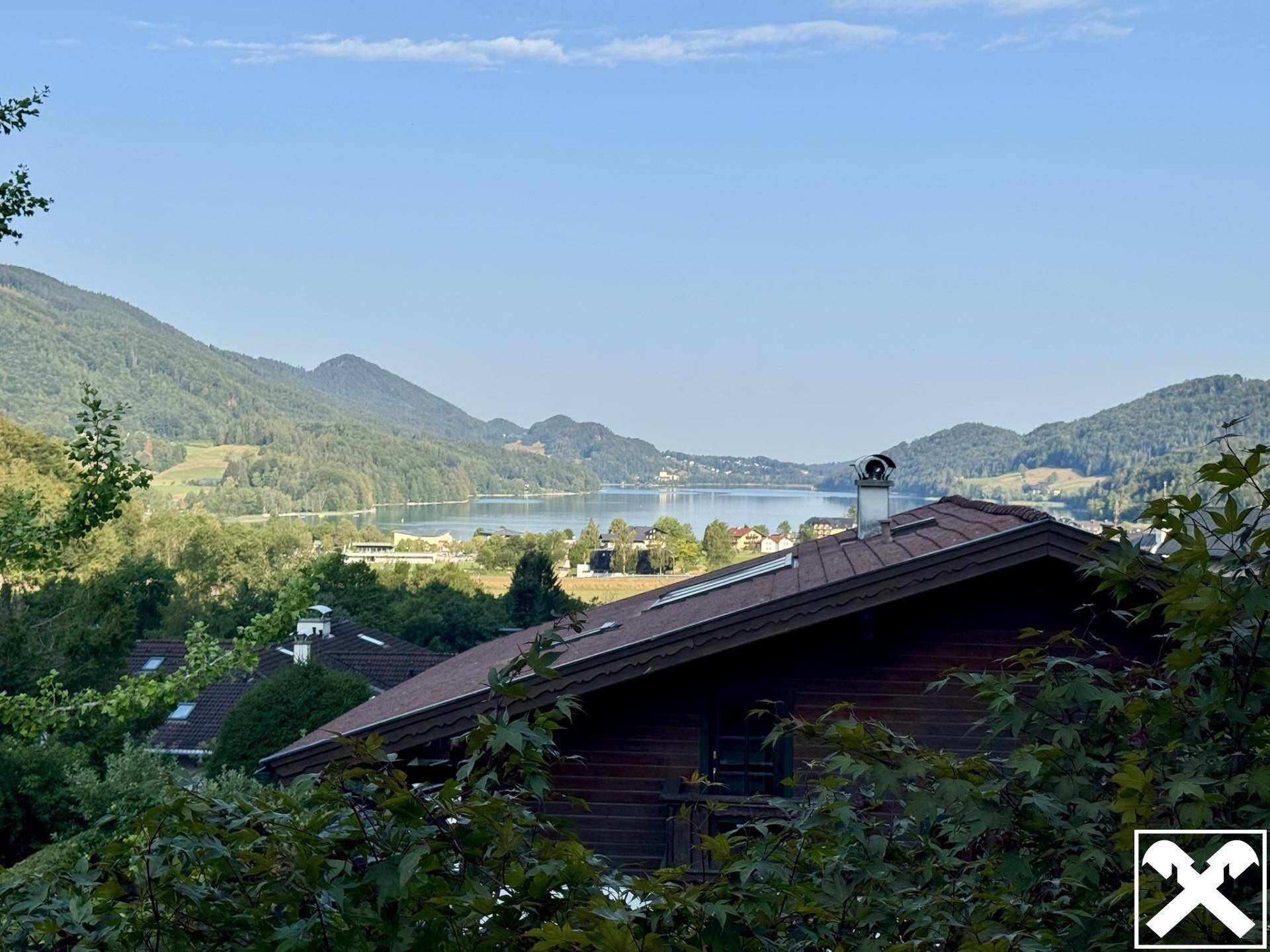 Malerischer Ausblick auf einen ruhigen See und die umliegende Berglandschaft über einem Hausdach.