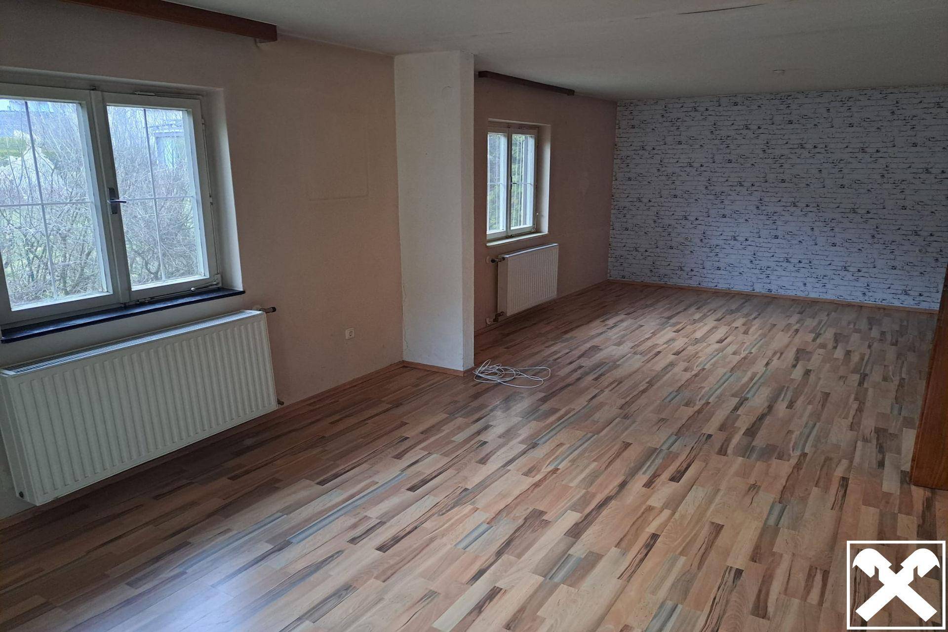 Heller Wohnraum mit Holzparkettboden, gemusterter Tapete und Blick ins Grüne.