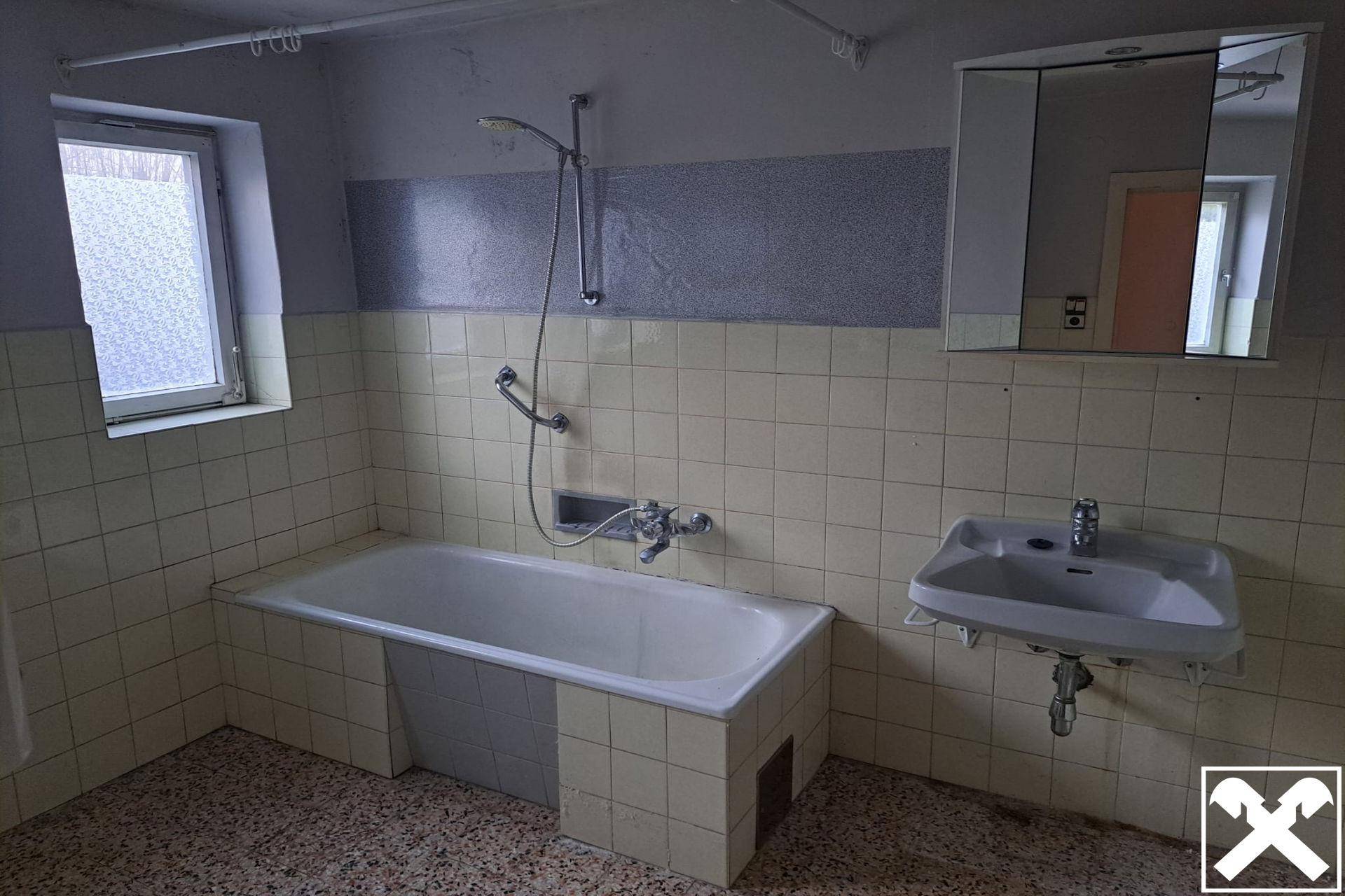Badezimmer mit Badewanne, Waschbecken, Spiegelschrank und Fenster.