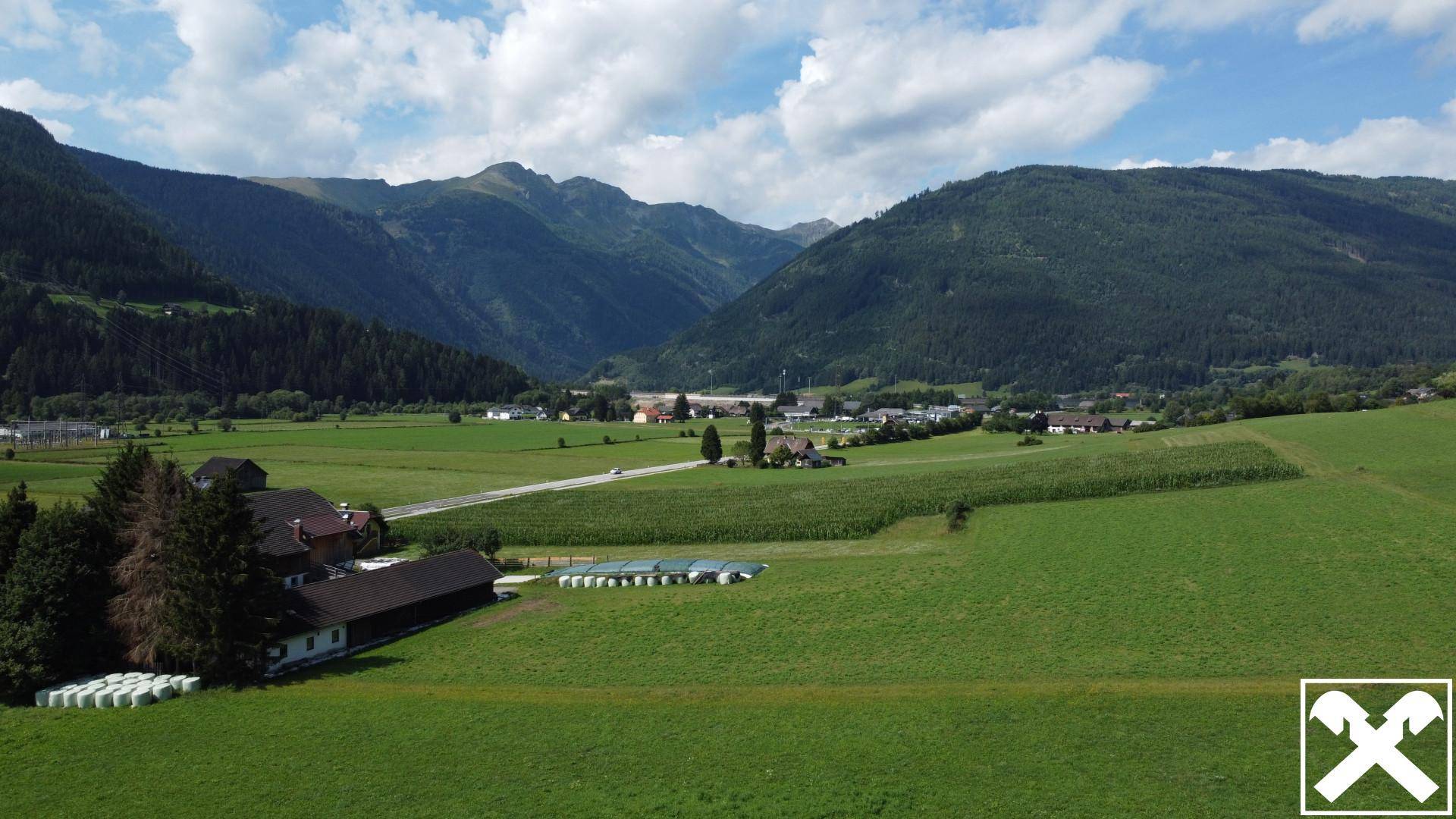 Weitläufige Landschaft mit grünen Feldern, bewaldeten Bergen und einem kleinen Dorf im Tal.