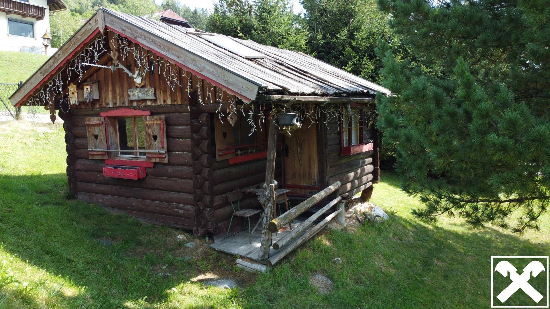 Rustikale Holzhütte mit traditioneller Dekoration und kleiner Veranda, eingebettet in grüne Natur.