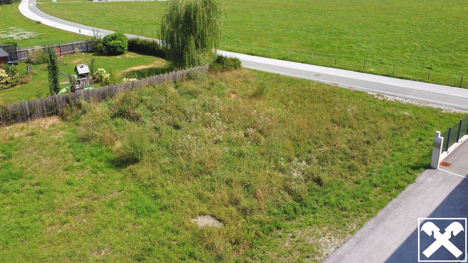 Luftaufnahme eines unbebauten Grundstücks mit angrenzender Straße und Nachbarhäusern.