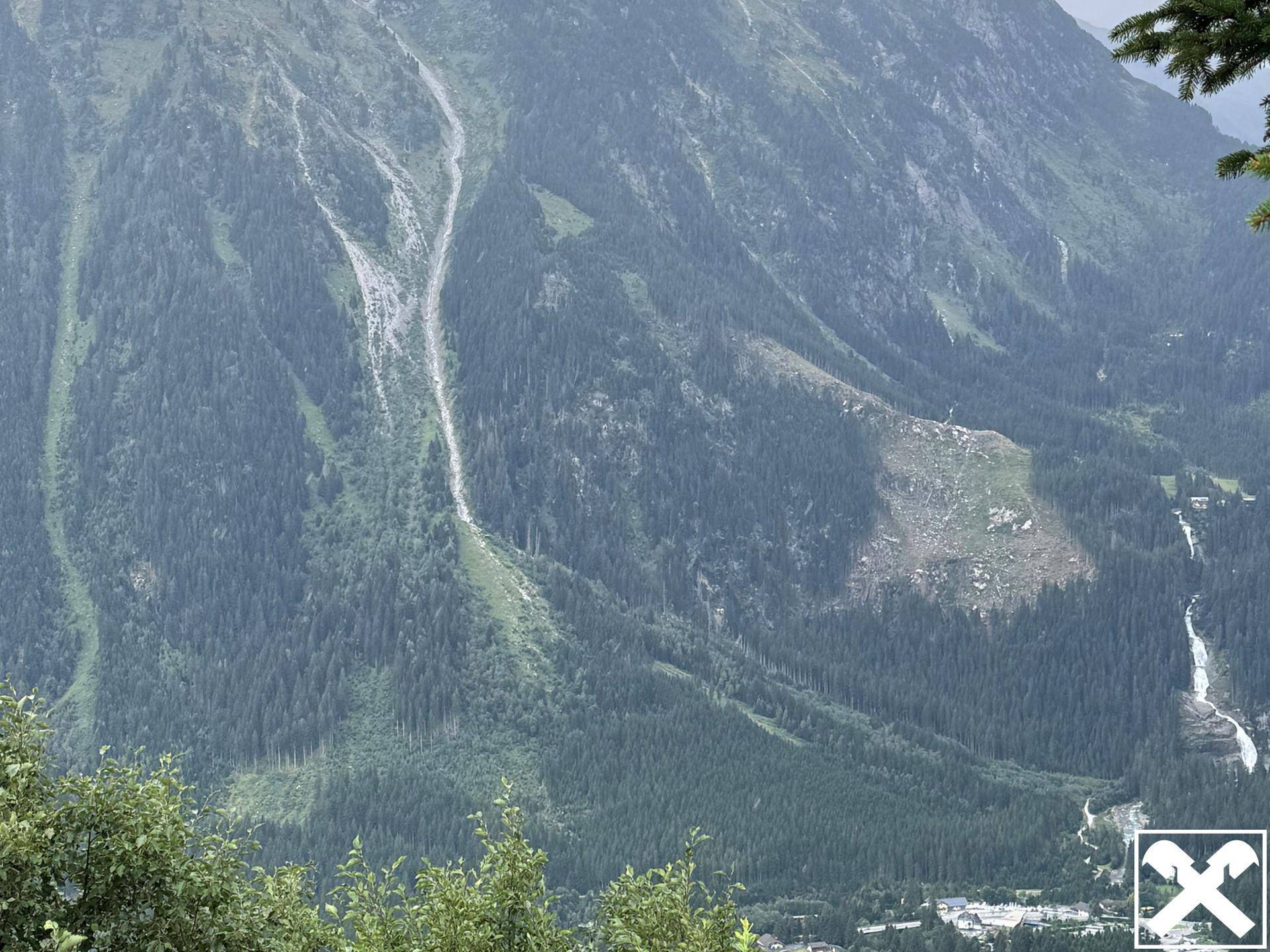 Weitläufige Ansicht einer majestätischen Berglandschaft mit dichten Wäldern, felsigen Abhängen und sichtbaren Wasserläufen, die ins Tal münden.