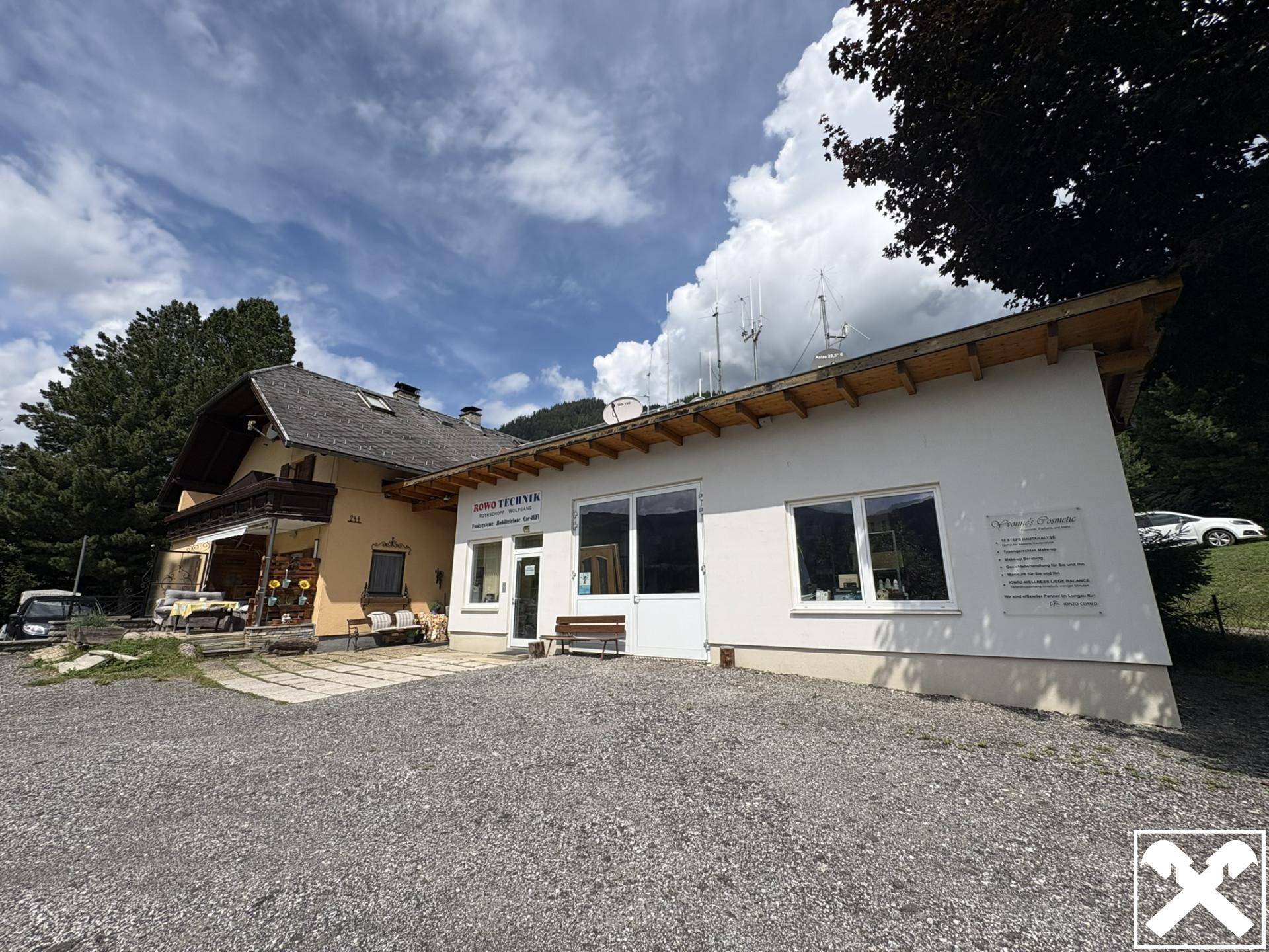 Ansicht des Gebäudes mit Geschäftseingang und Wohnbereich, umgeben von Natur und Bergen.
