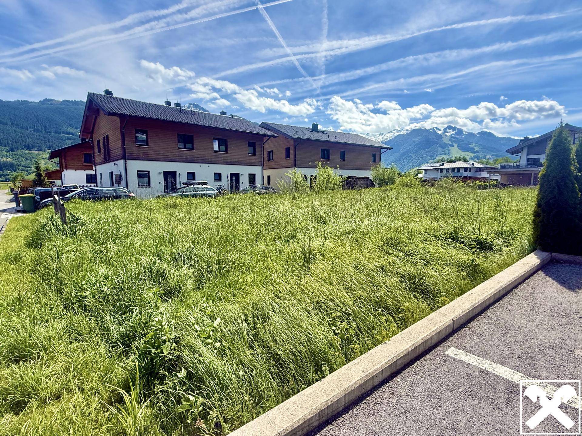 Grünes Baugrundstück mit Blick auf traditionelle Häuser und die umliegende Berglandschaft.