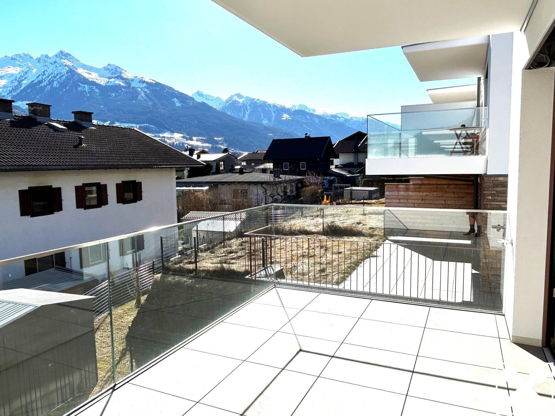 Geräumiger Balkon mit Glasbrüstung, Fliesenboden und beeindruckendem Bergblick.