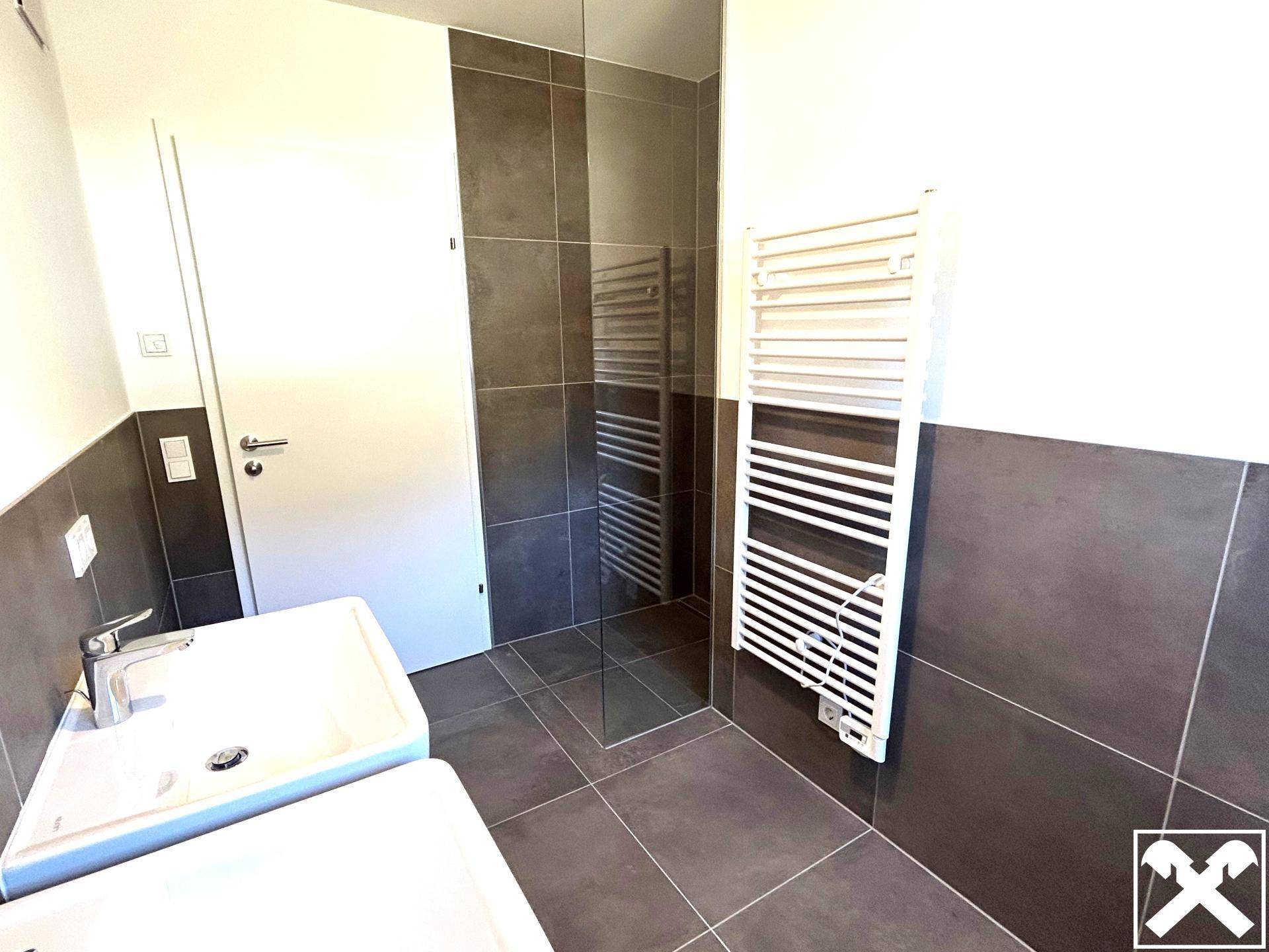 Modernes Badezimmer mit dunklen Fliesen, weißem Waschbecken und beheiztem Handtuchhalter.