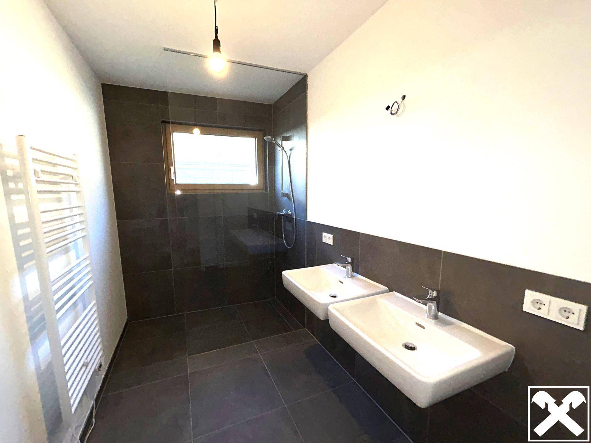 Modernes Badezimmer mit dunklen Fliesen, Doppelwaschbecken, Dusche und Fenster.
