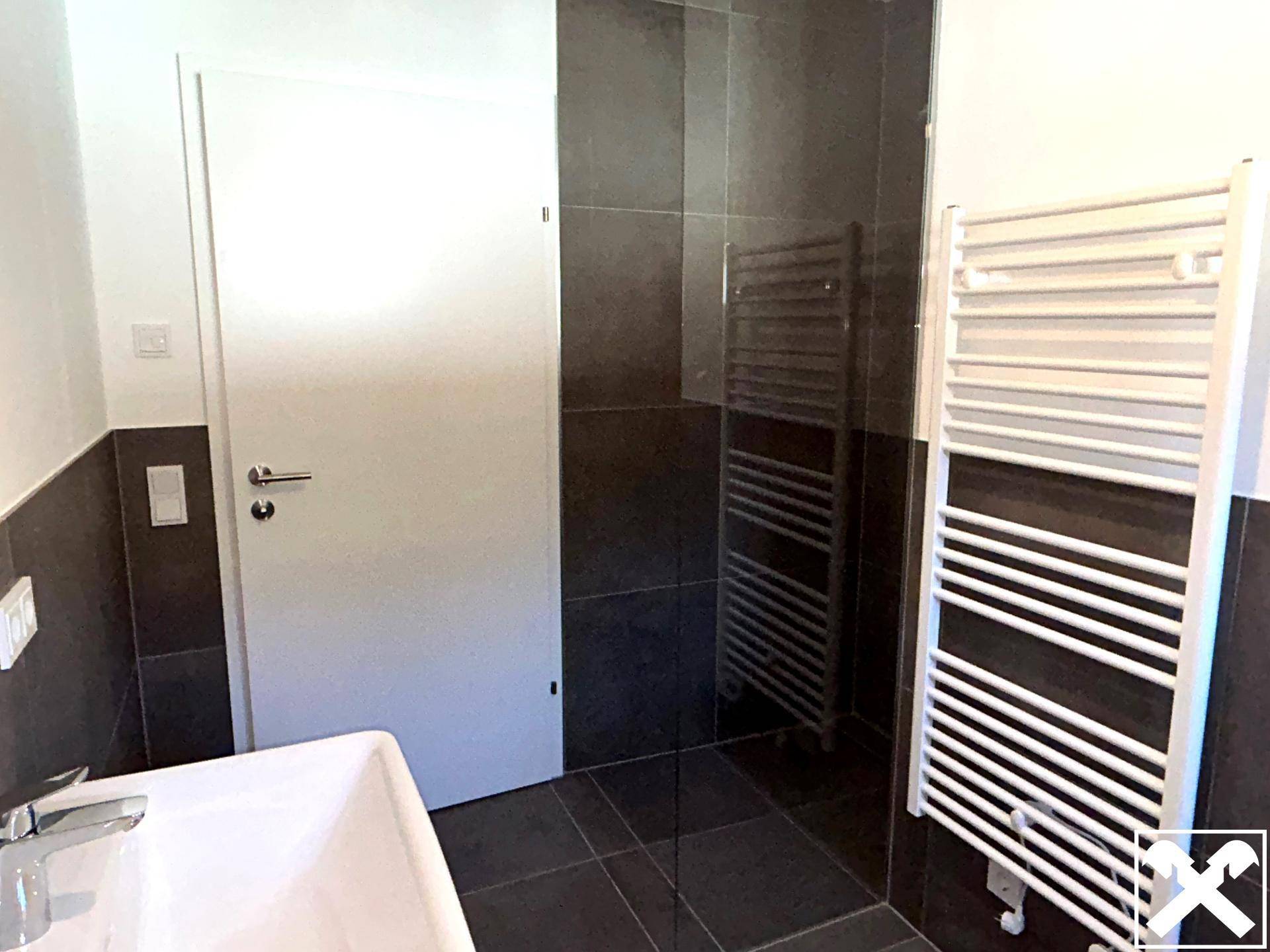 Modernes Badezimmer mit dunklen Fliesen, weißem Waschbecken und beheiztem Handtuchhalter.