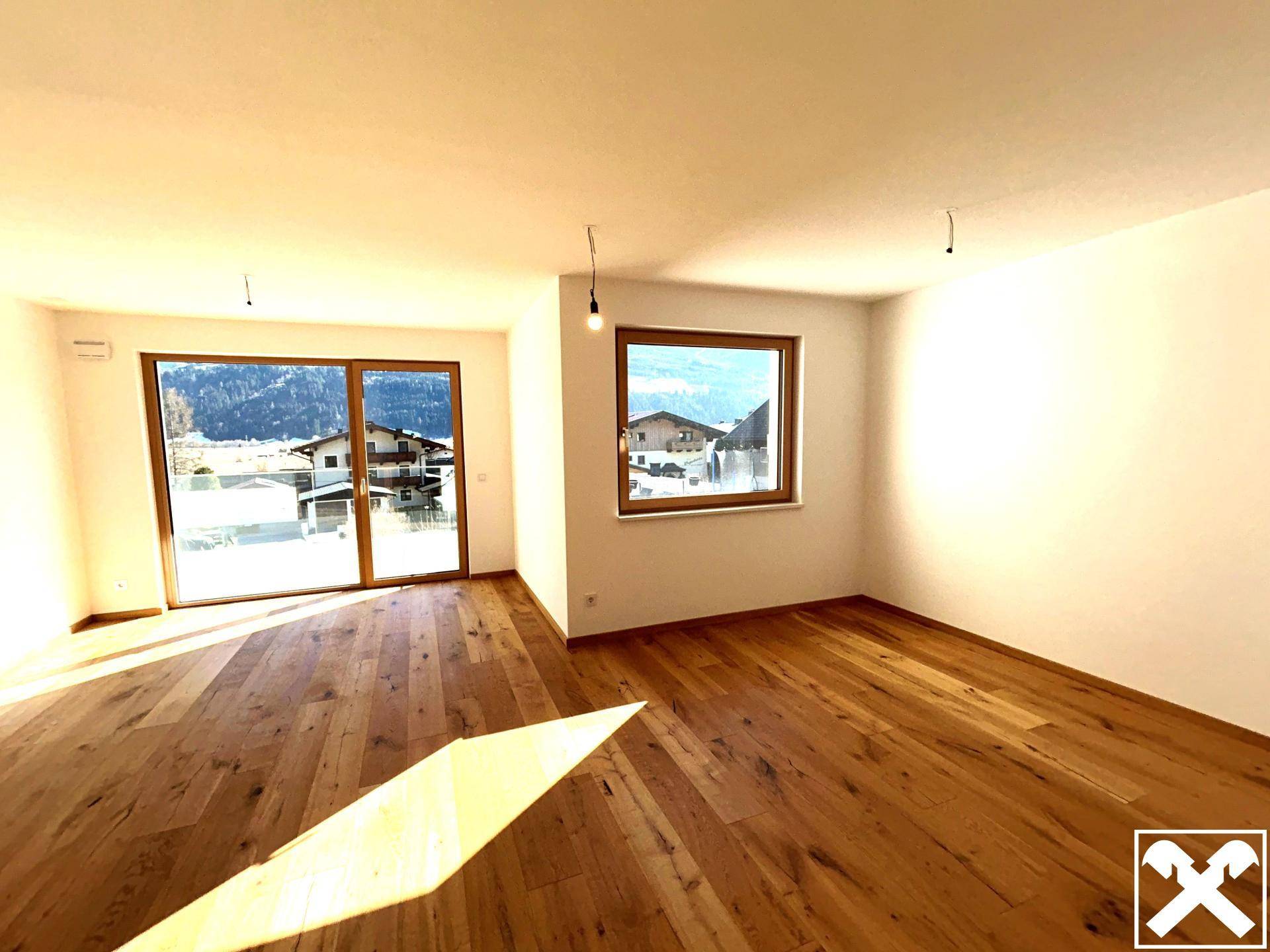 Heller Wohnraum mit hochwertigem Holzparkettboden und Zugang zu einem Balkon mit Bergblick.
