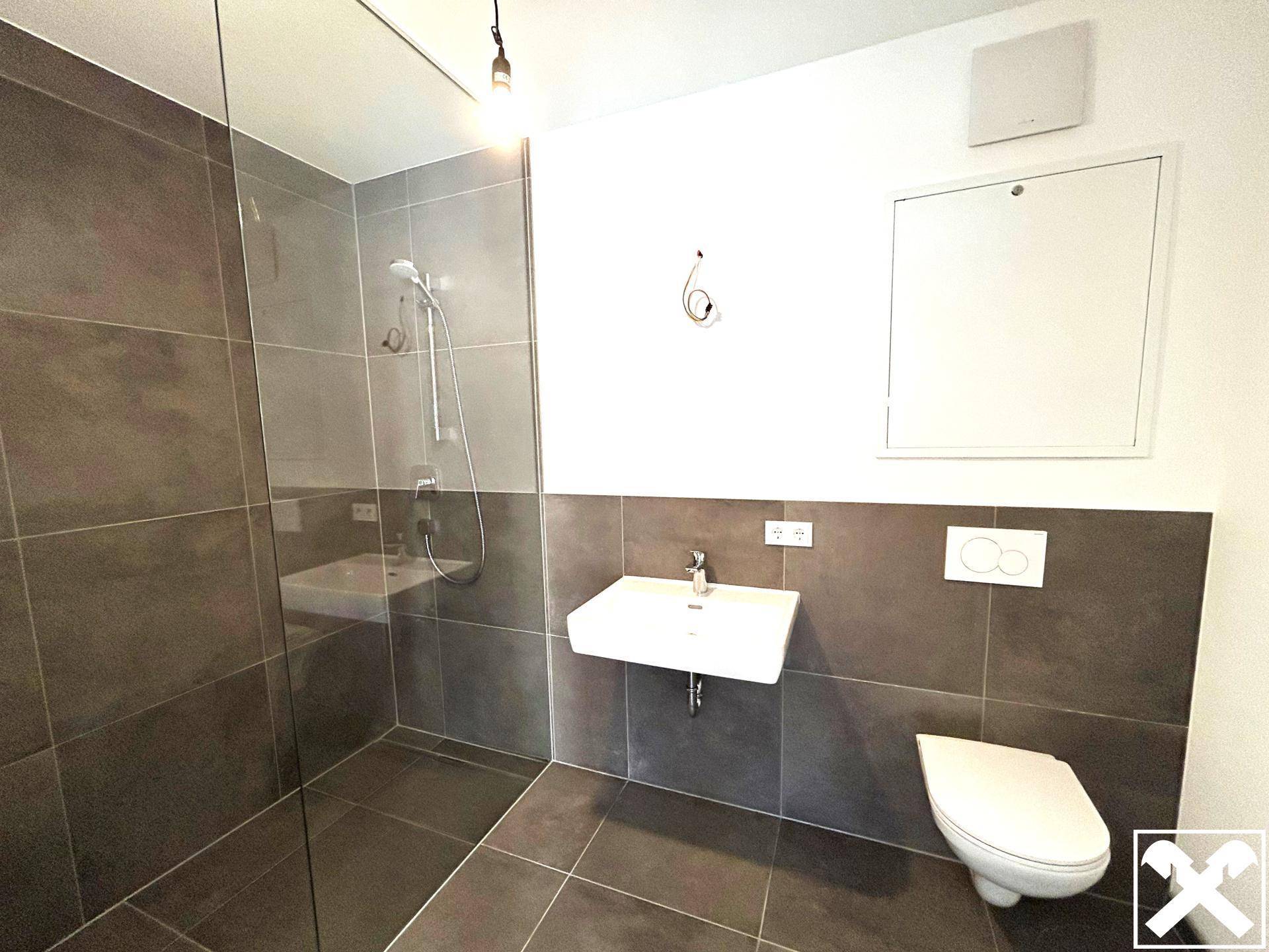 Modernes Badezimmer mit dunklen Fliesen, einer begehbaren Dusche und einem wandhängenden WC.
