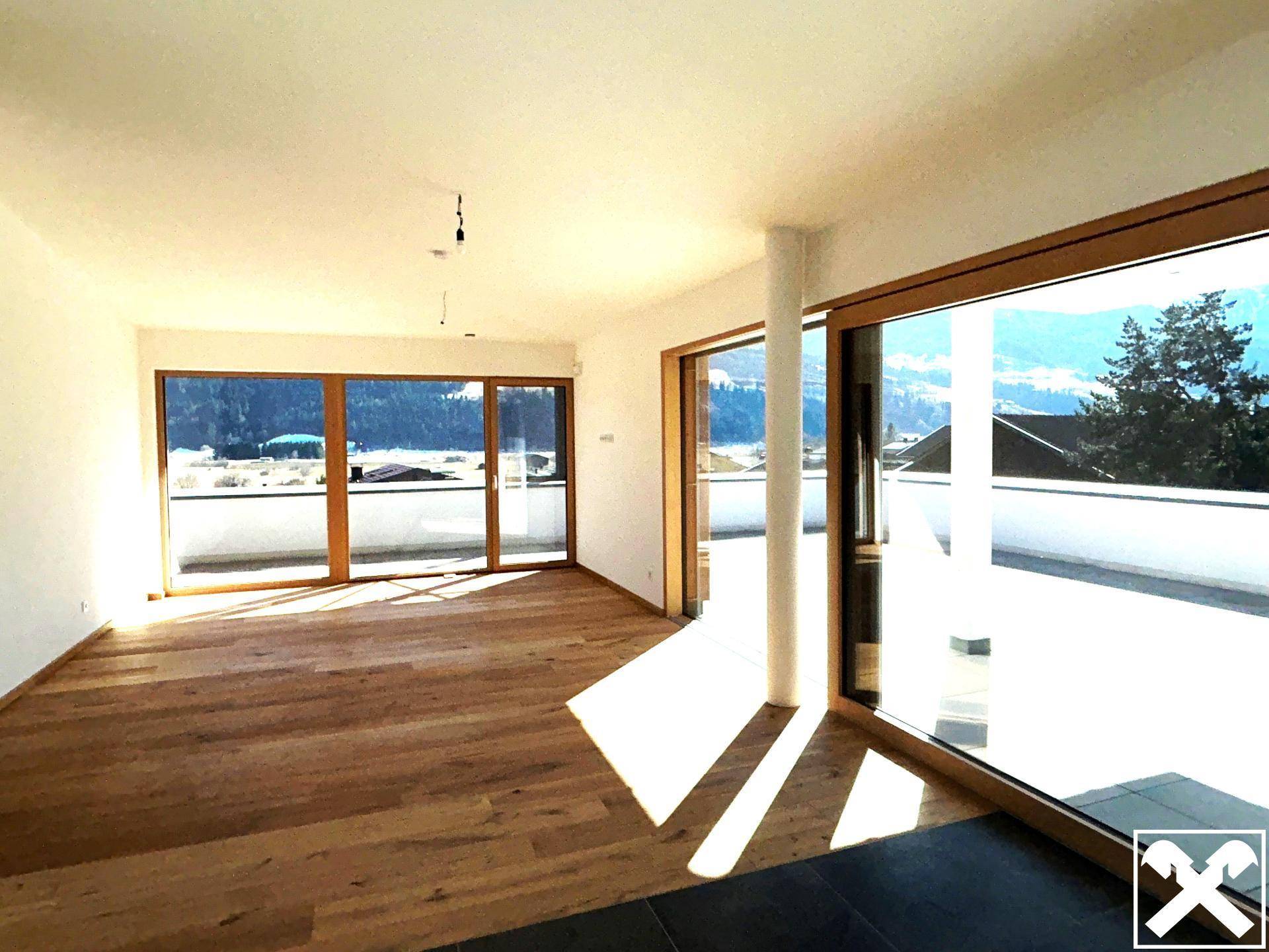 Lichtdurchfluteter Raum mit Holzboden und großen Fenstern, die einen weiten Bergblick bieten.