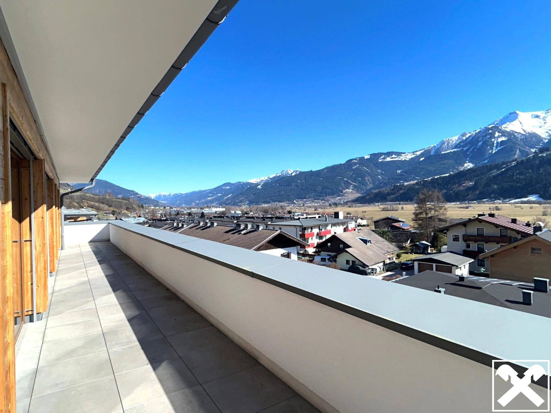 Langer Balkon mit Fliesenboden und weitem Blick über das Tal und die schneebedeckten Berge.