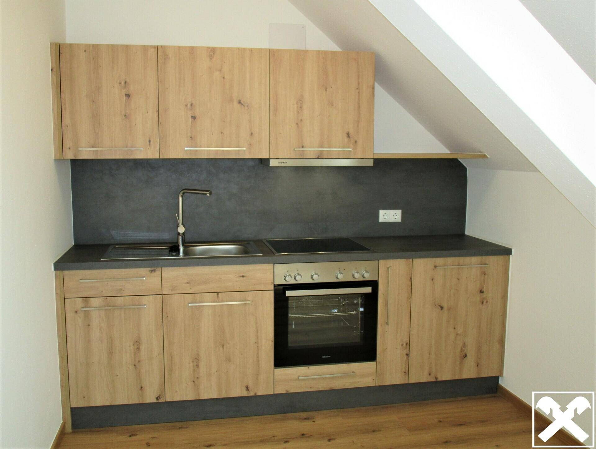 Kompakte Einbauküche mit Holzdekorfronten, Kochfeld, Backofen und Dachschräge.