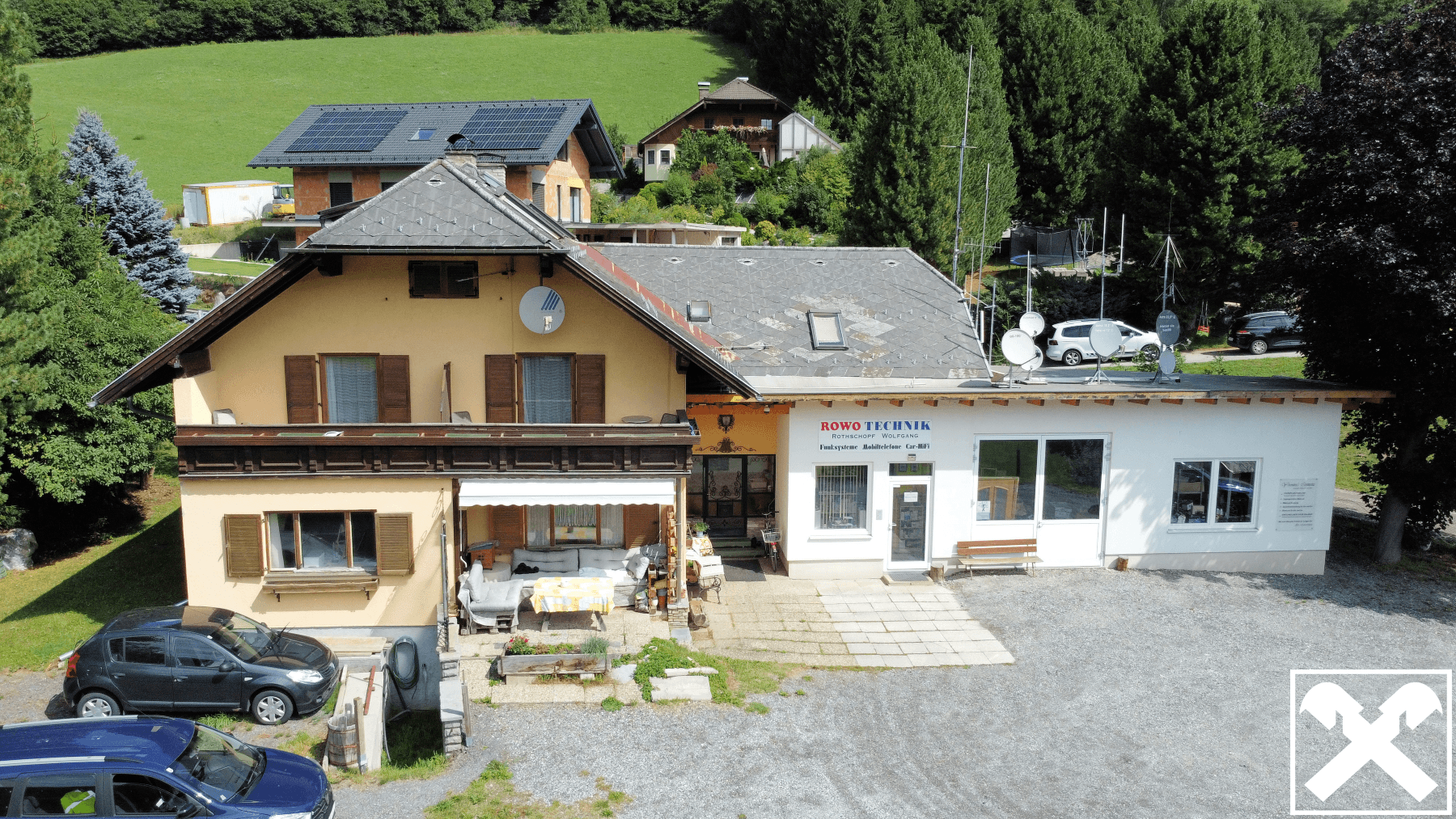 Luftaufnahme eines Wohnhauses mit angrenzendem Geschäft und Parkplätzen in ländlicher Umgebung.