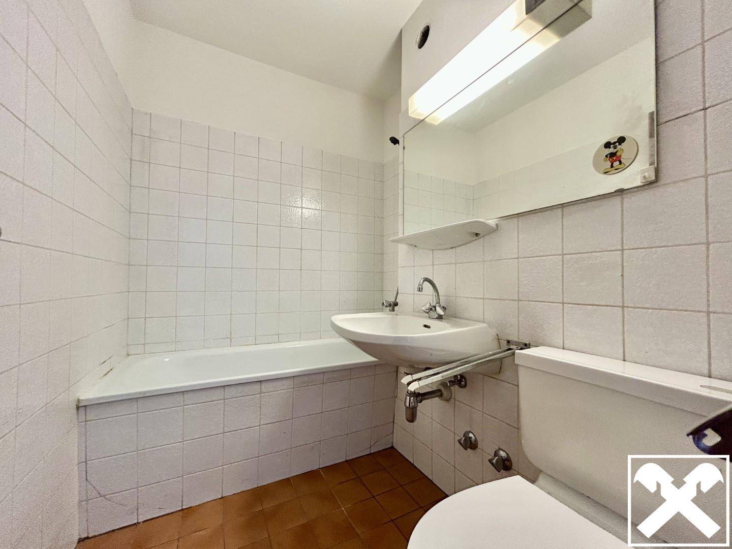 Badezimmer mit weißen Fliesen, Badewanne, Toilette und Waschbecken mit einem Spiegel darüber.