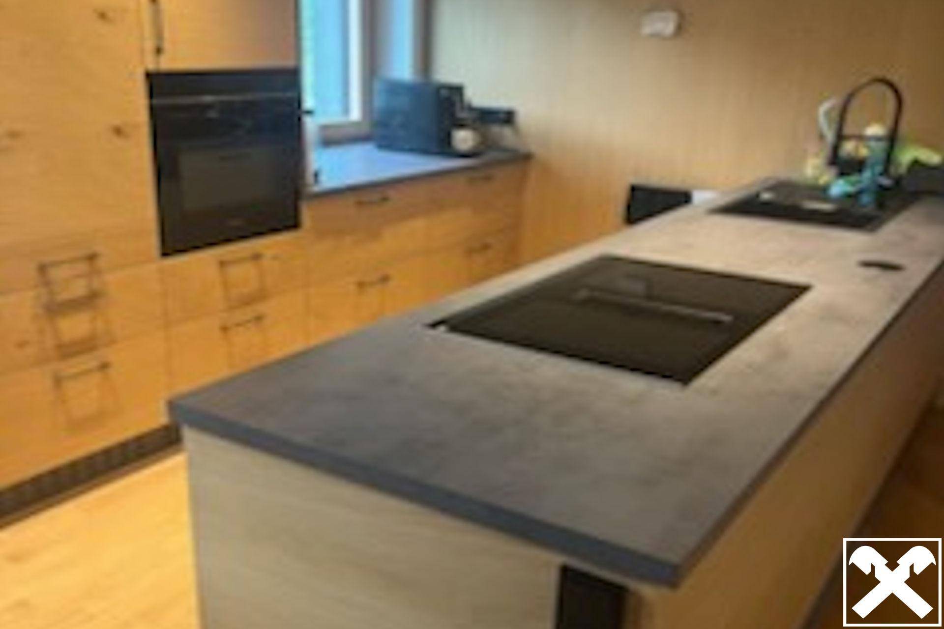 Moderne Küche mit hellen Holzschränken, dunkler Arbeitsplatte und integriertem Kochfeld.