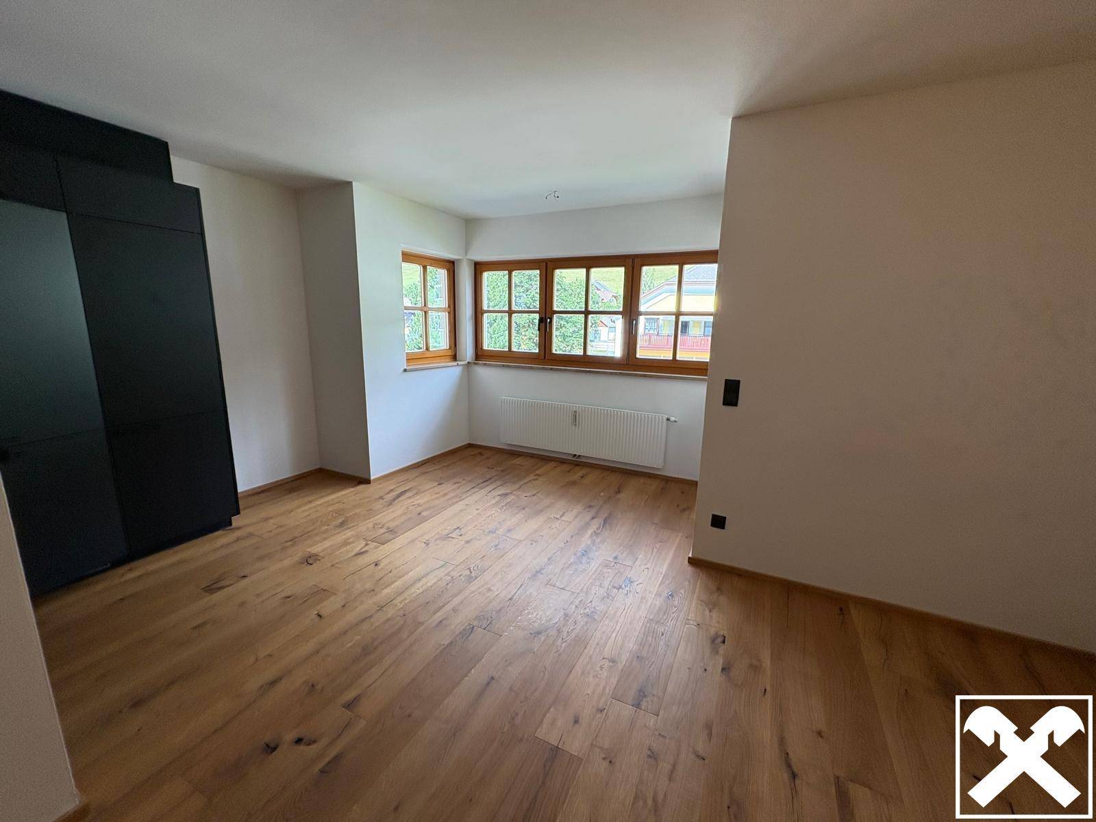 Geräumiges Zimmer mit Holzboden und großen Fenstern, die viel Tageslicht hereinlassen.