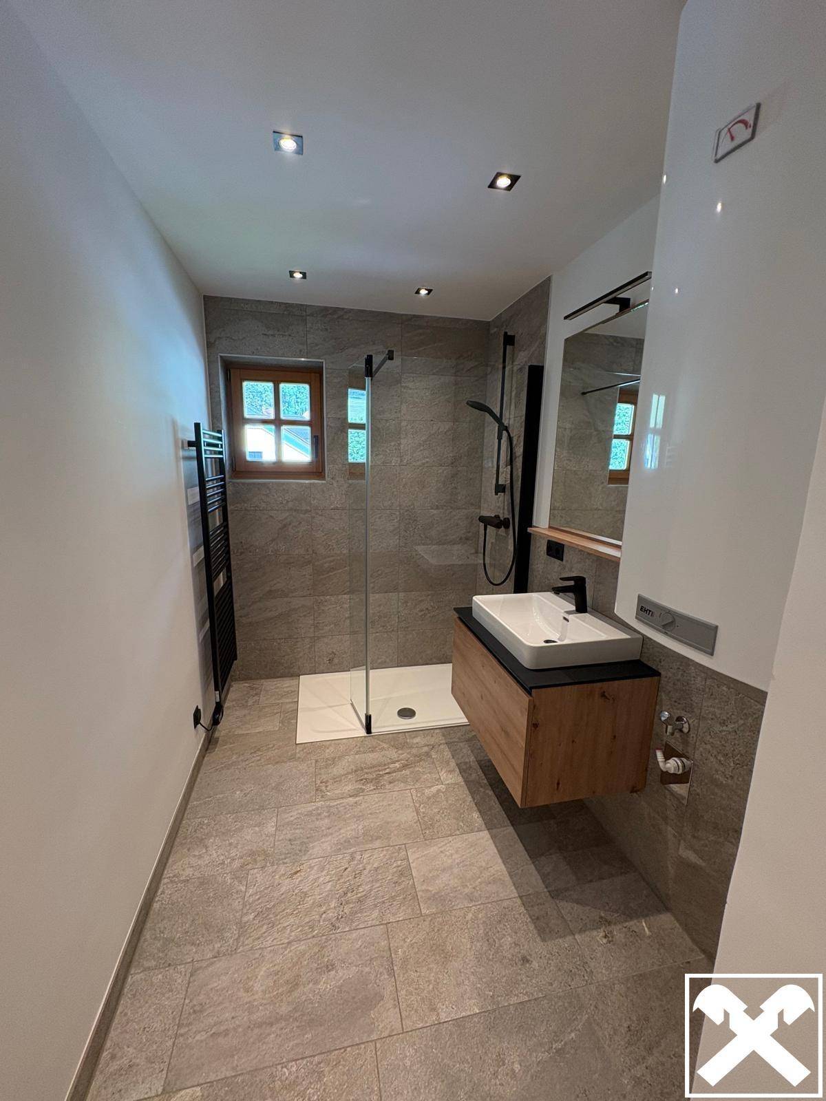 Modernes Badezimmer mit grauen Fliesen, begehbarer Dusche und Holzwaschtisch.