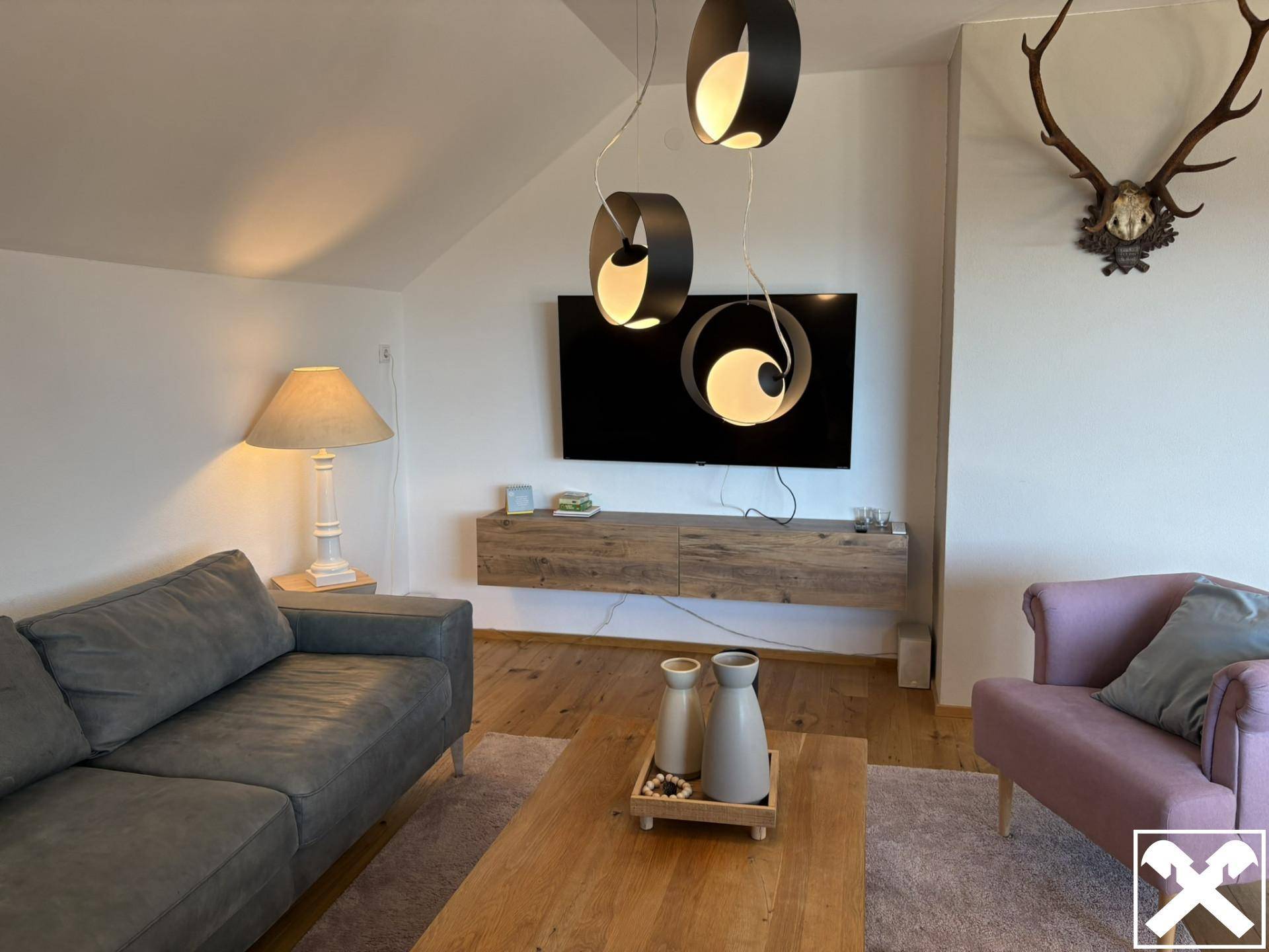 Gemütliches Wohnzimmer im Dachgeschoss mit Holzboden, modernem TV-Bereich und Hirschgeweih-Dekoration.