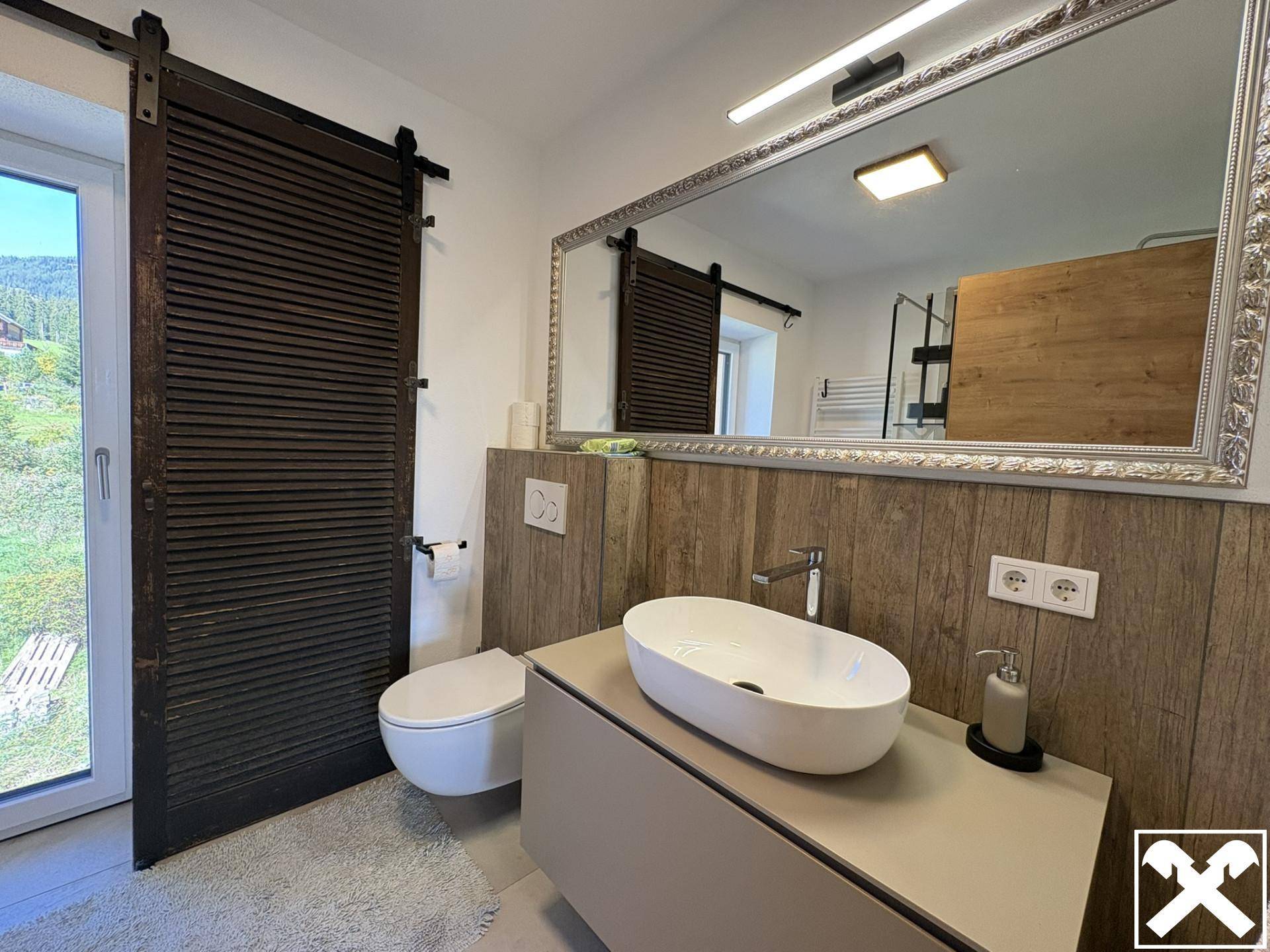 Modernes Badezimmer mit Holzakzenten, großem Spiegel, stilvollem Waschbecken und Schiebetür.