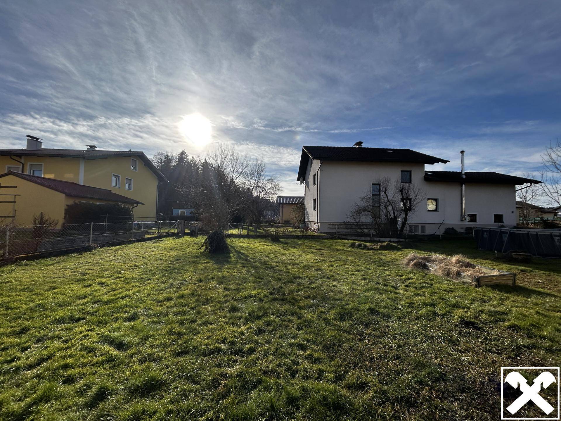 Sonniger Garten mit weitem Rasen und Blick auf die Nachbarschaft bei tiefstehender Sonne.