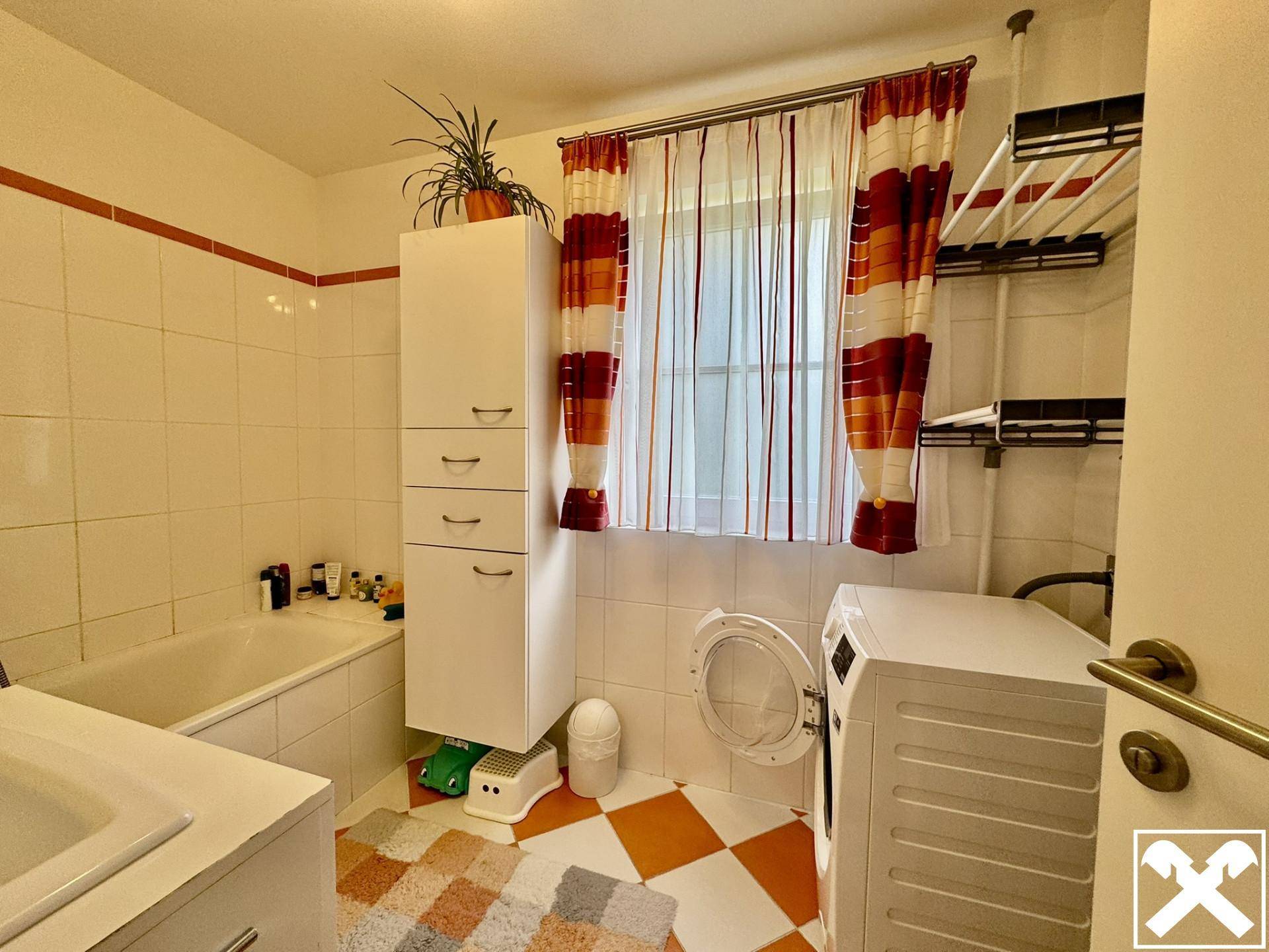 Funktionales Badezimmer mit Badewanne, Waschmaschine und Fenster für Tageslicht.
