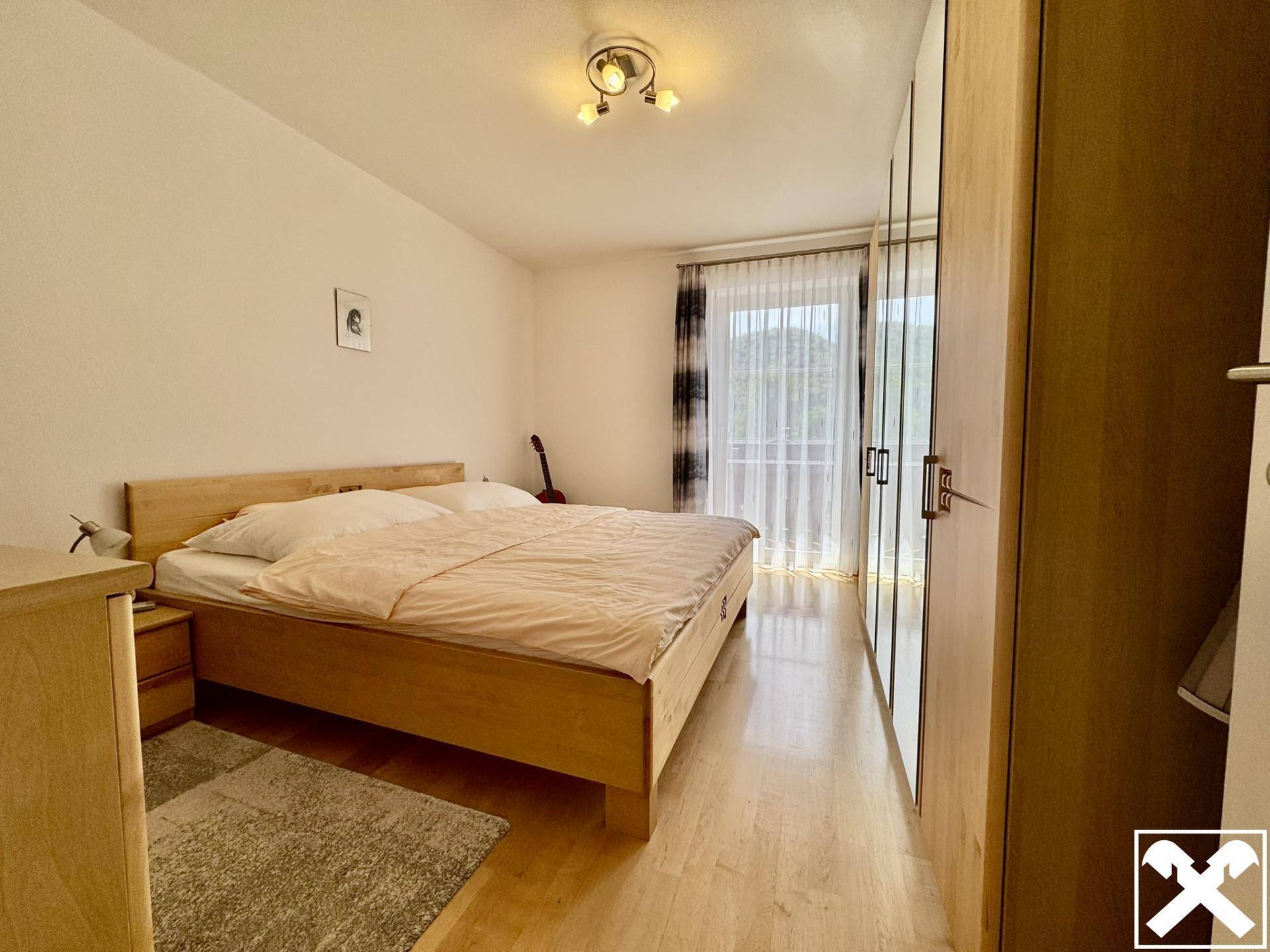 Helles Schlafzimmer mit Holzbett, großem Kleiderschrank und Zugang zu einem Balkon.