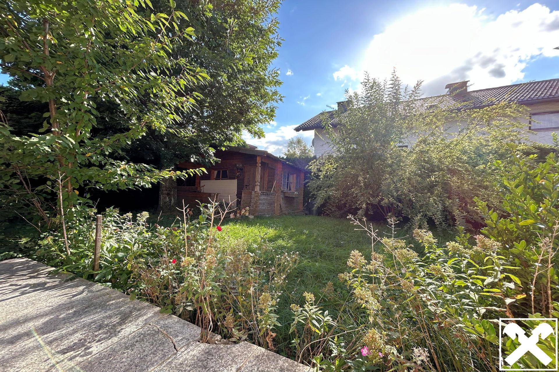 Großer, sonniger Gartenbereich mit Rasen, Bäumen und einem kleinen Gartenhaus.