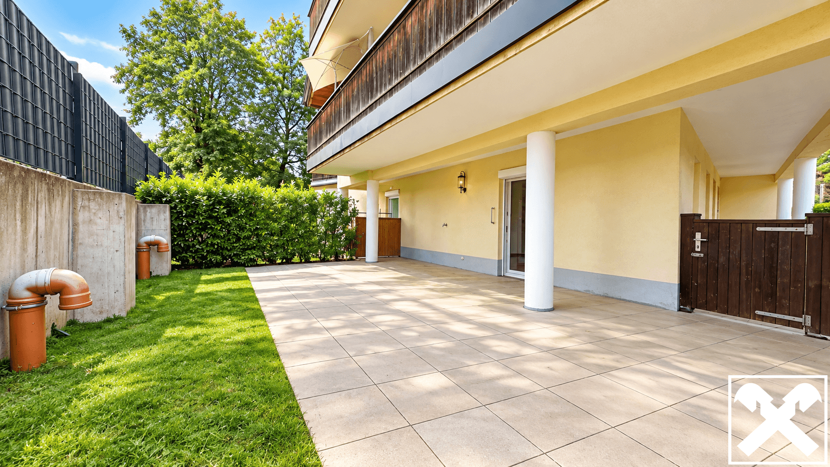 Große gepflasterte Terrasse mit angrenzendem Rasenbereich und einer grünen Hecke.
