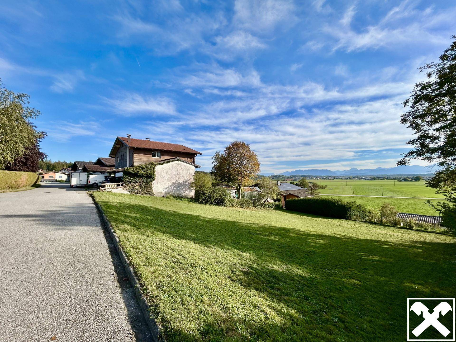 Blick auf ein Wohnhaus mit Zufahrt und weitem Ausblick über Felder und die Bergkette am Horizont.