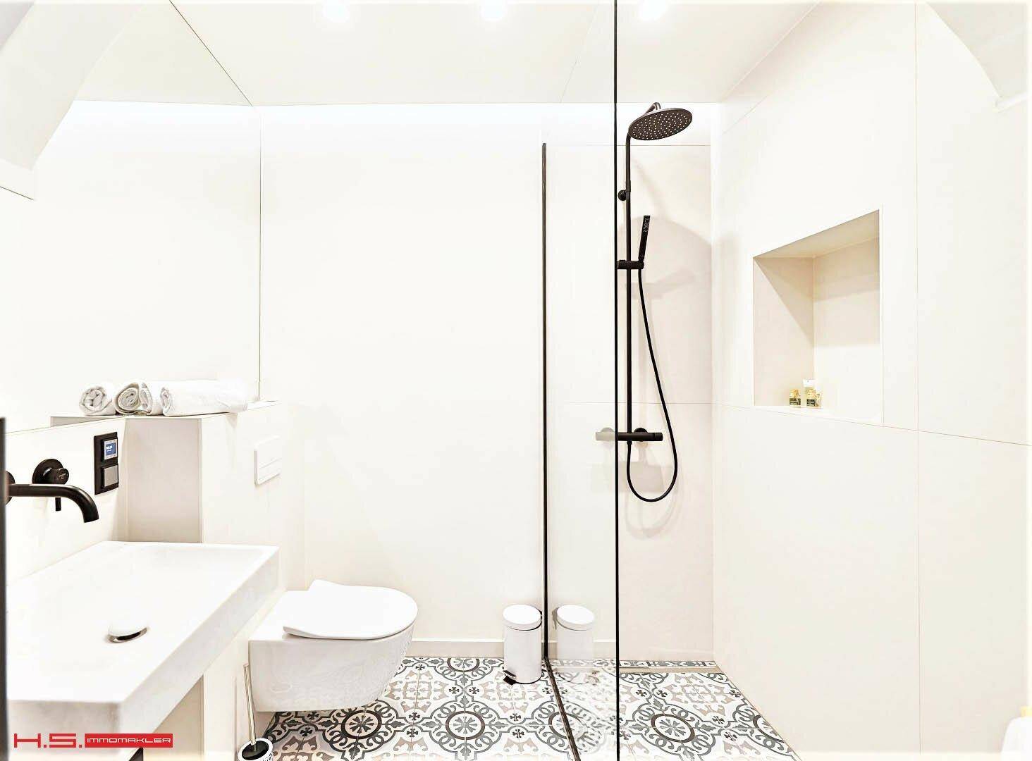 Modernes Badezimmer mit wandhängendem WC, Waschbecken und begehbarer Dusche auf gemusterten Fliesen.